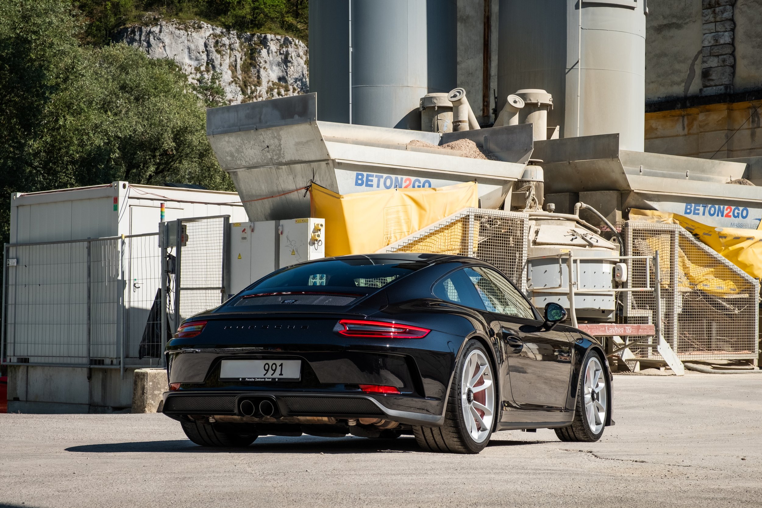 Ein schwarzer Porsche 911 Sportwagen vor einer Baustelle mit Baufahrzeugen und Sicherheitszäunen.