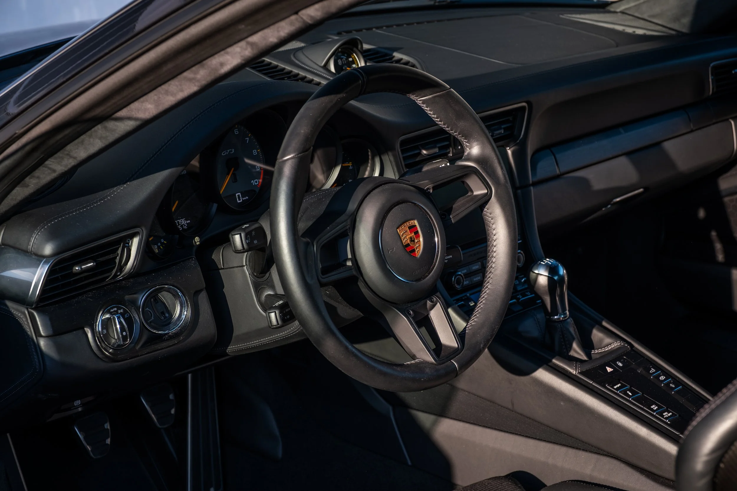 Innenraum eines Porsche-Sportwagens mit Lenkrad, Dashboard, Schalthebel und Bedienfeld.