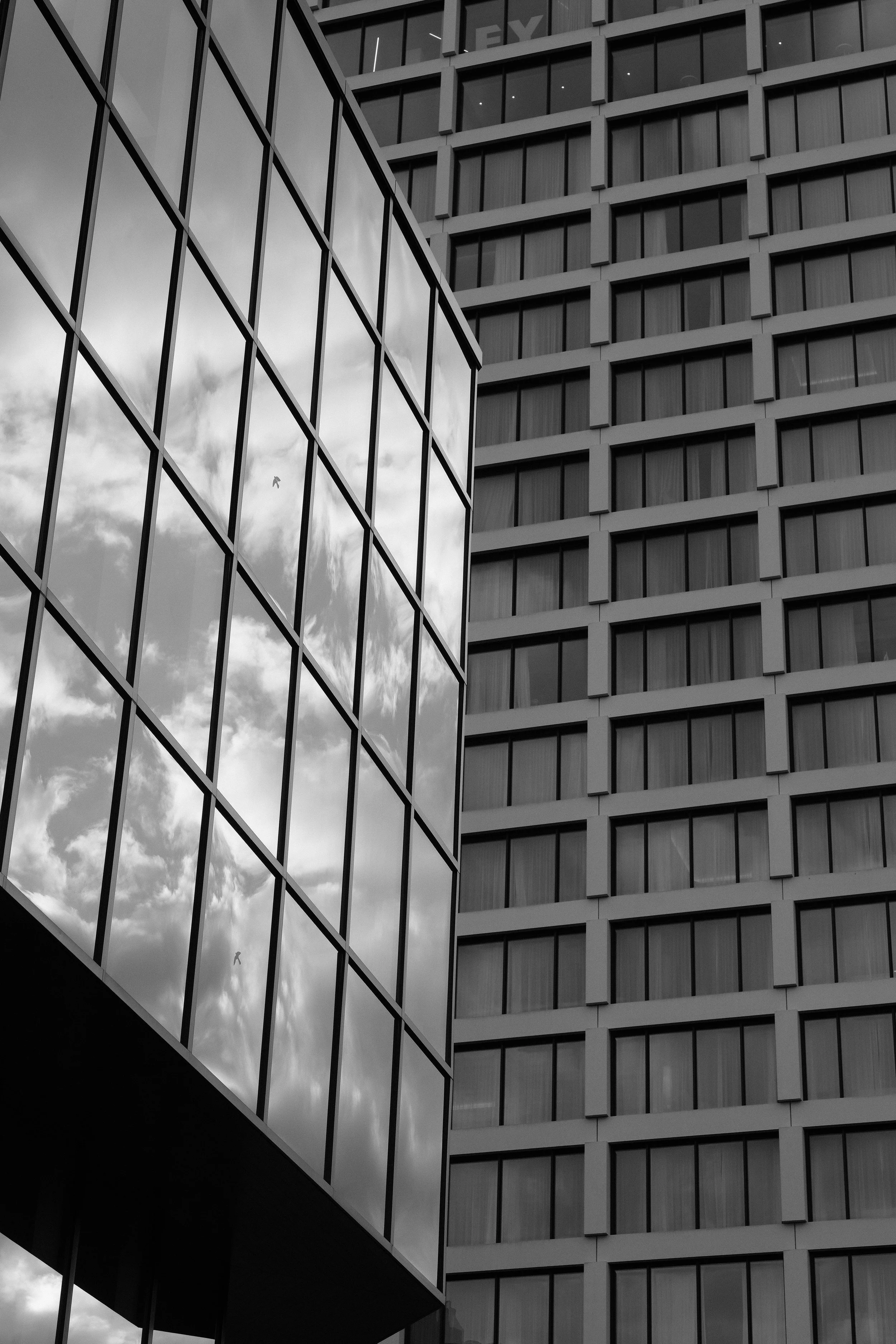 Schwarz-Weiß-Aufnahme von modernen Bürobauten mit großen Fenstern, die den Himmel und Wolken spiegeln.