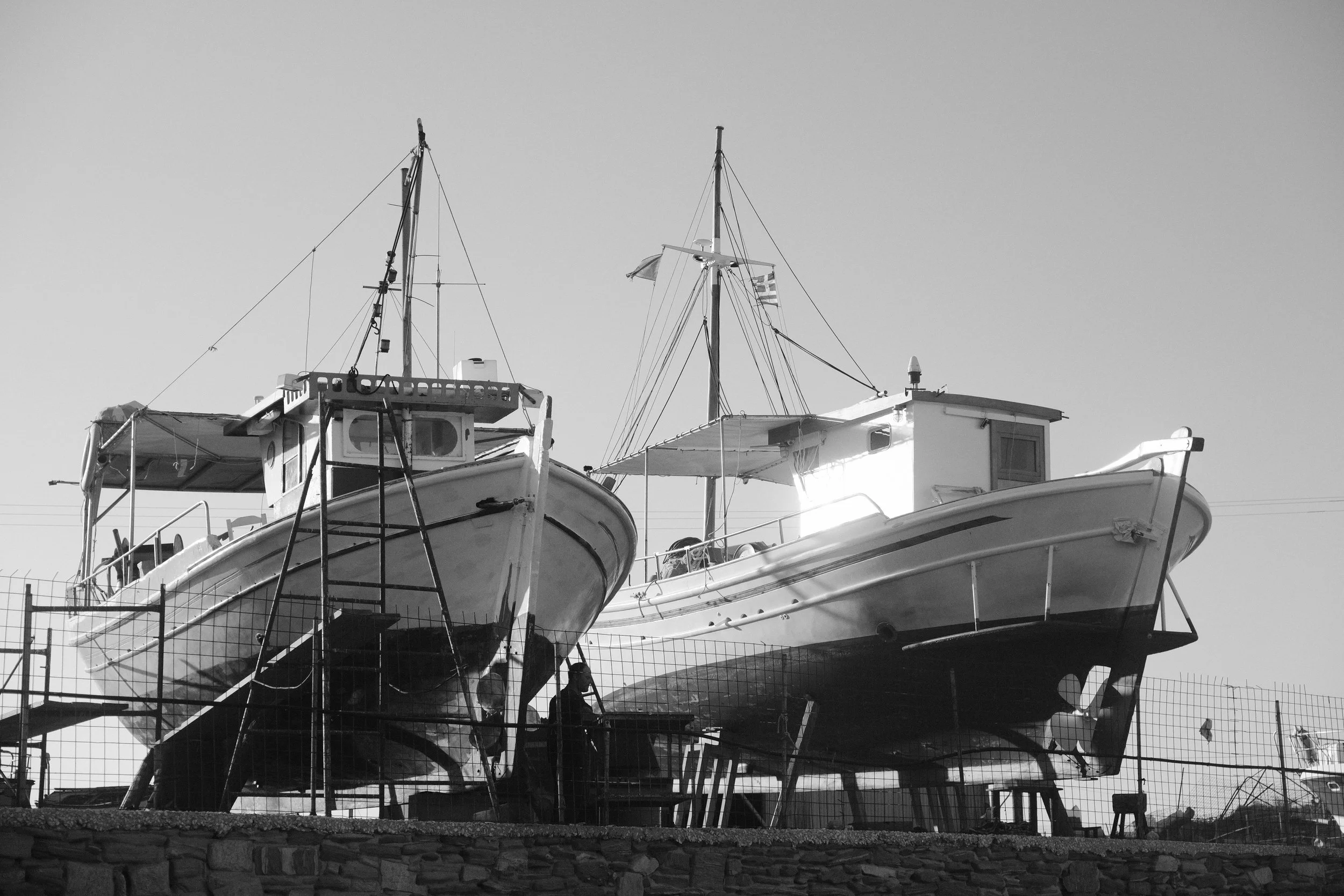 Zwei Boote auf Land, eingezäunt, im Hintergrund ein klarer Himmel.
