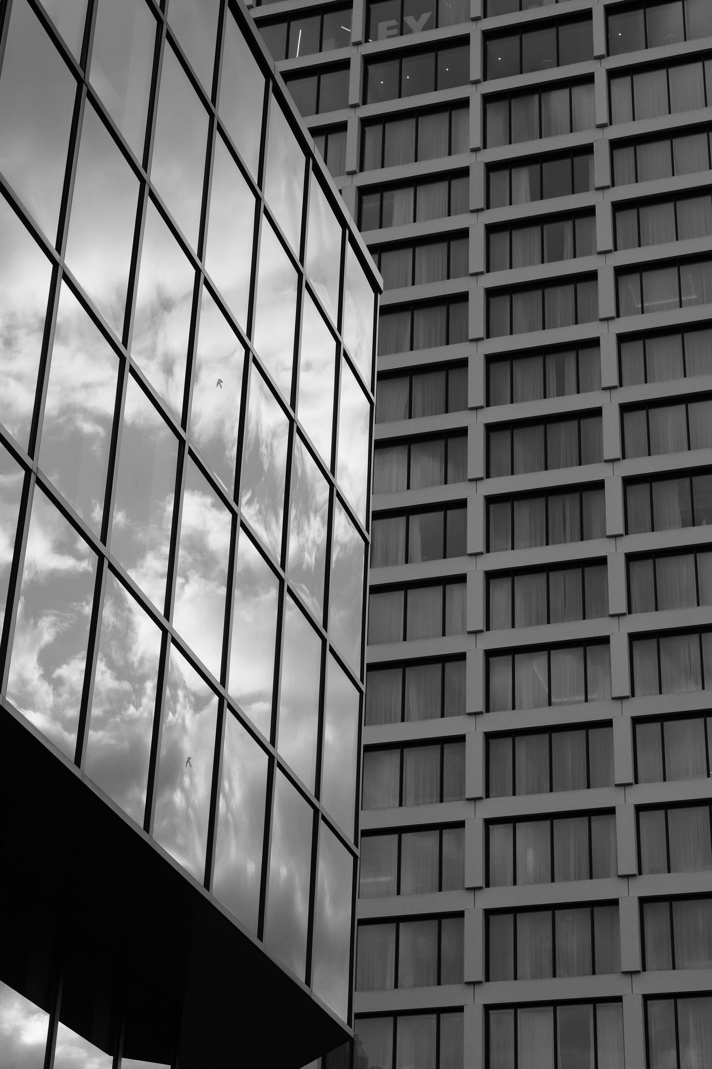 Zwei moderne Hochhäuser mit Glasfassaden, die den Himmel und Wolken spiegeln, in schwarz-weiß.