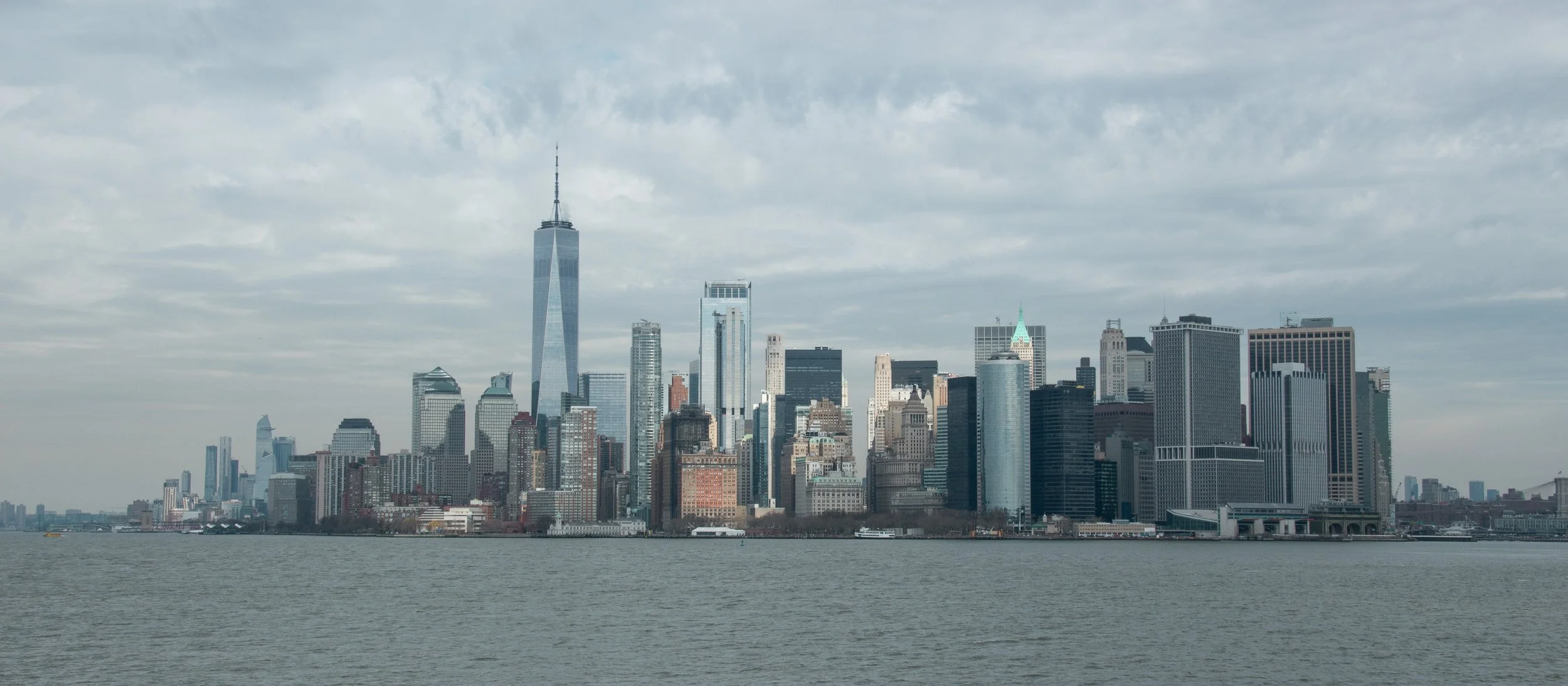 Stadt skyline von New York City mit Hochhäusern und Wasser im Vordergrund, bewölkter Himmel.