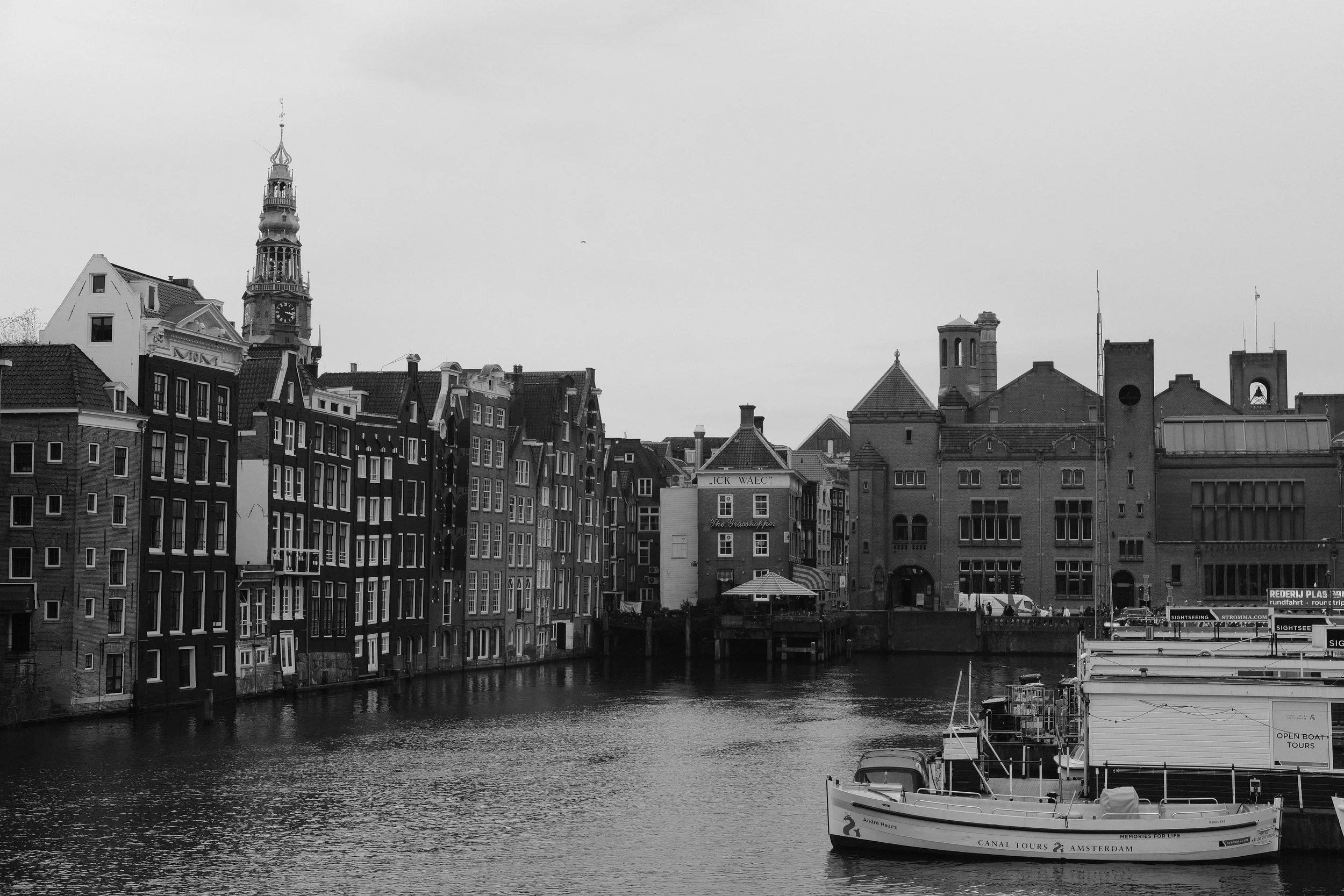 Schwarz-weiß-Foto von einem Kanal in Amsterdam mit historischen Gebäuden und Booten.