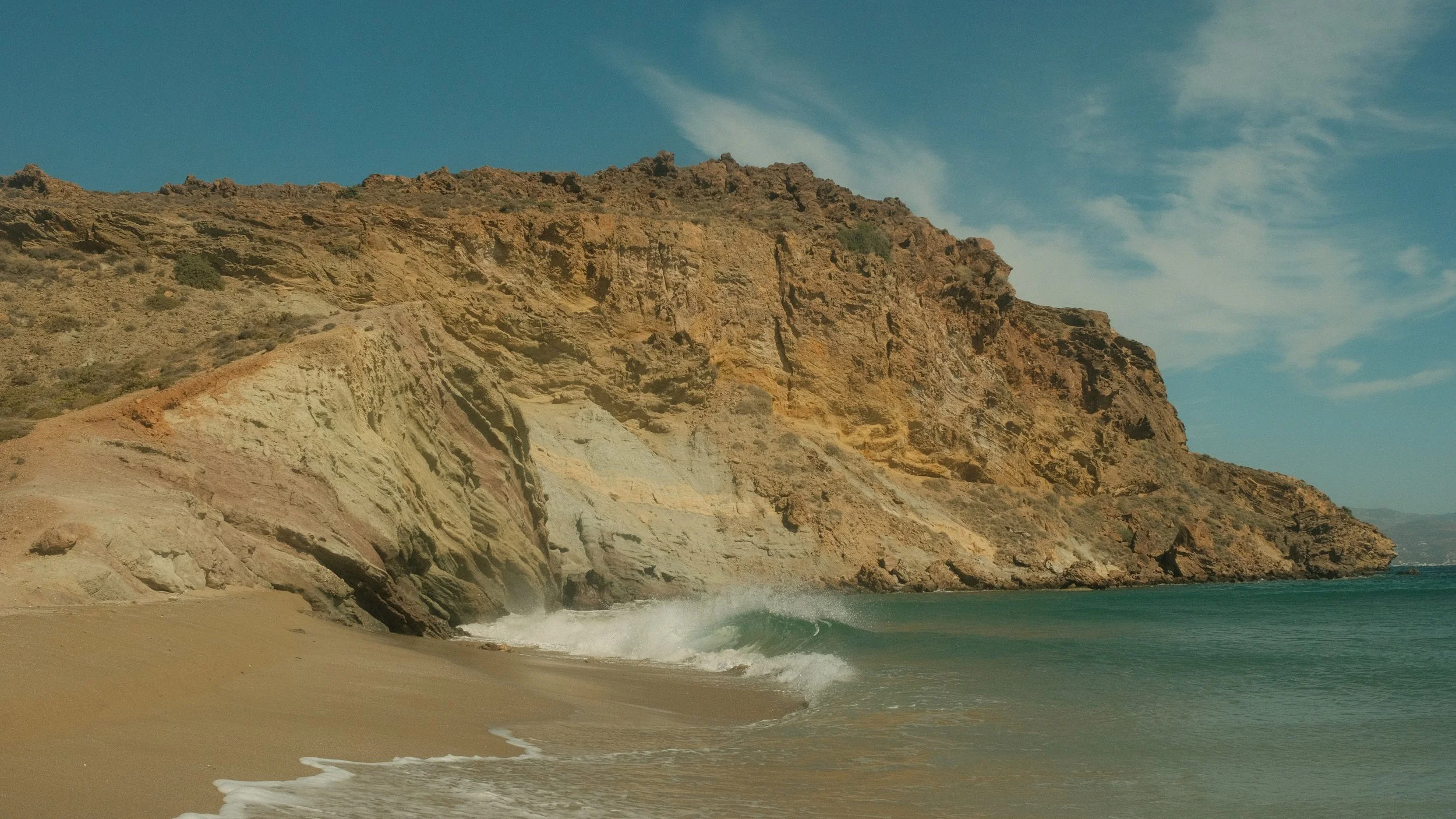Strand mit Felsen und Wellen im Meer bei sonnigem Himmel.