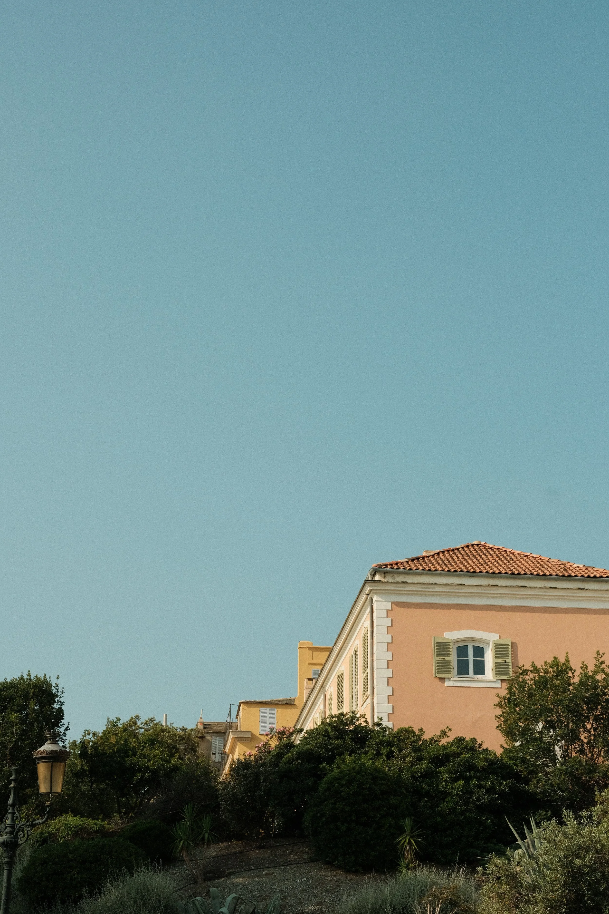 Ein Haus mit orangefarbener Fassade, grünen Fensterläden und roten Ziegeln, umgeben von Bäumen und einem bewölkten Himmel.