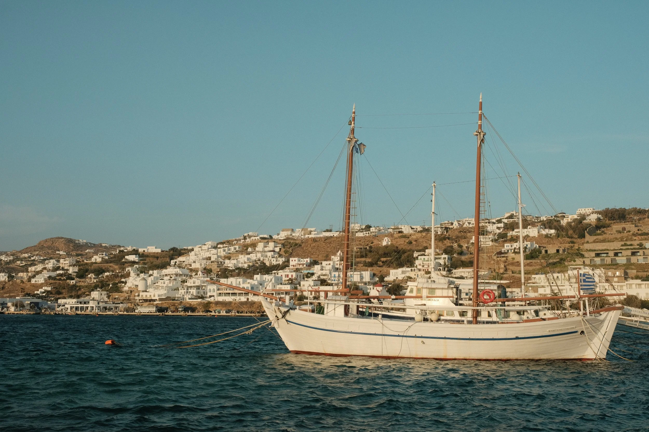 Ein Segelboot liegt im Wasser vor einer Küste mit weißen Häusern auf Hügeln.