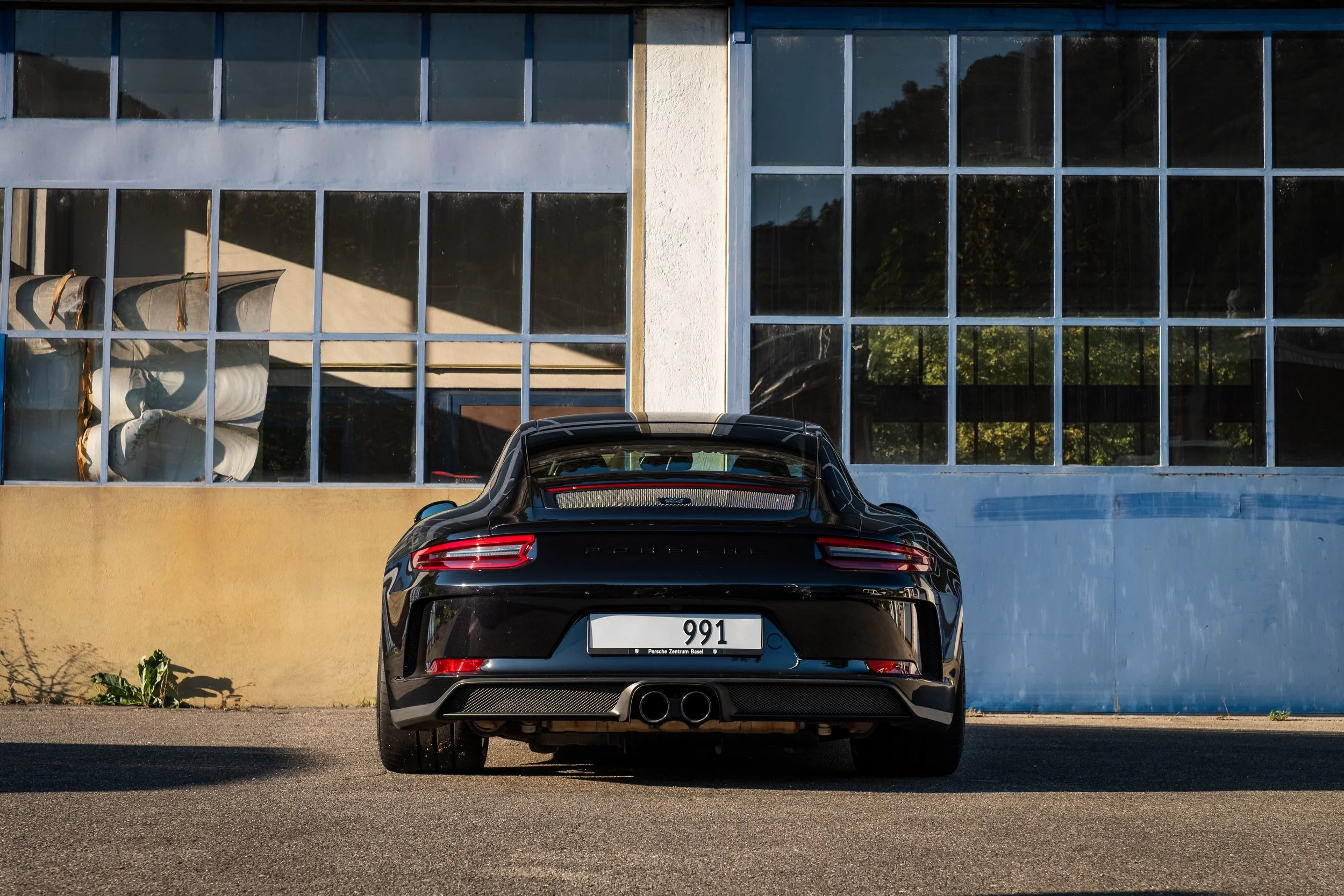Schwarzer Porsche 911 vor einem Gebäude mit großen Fensterflächen.