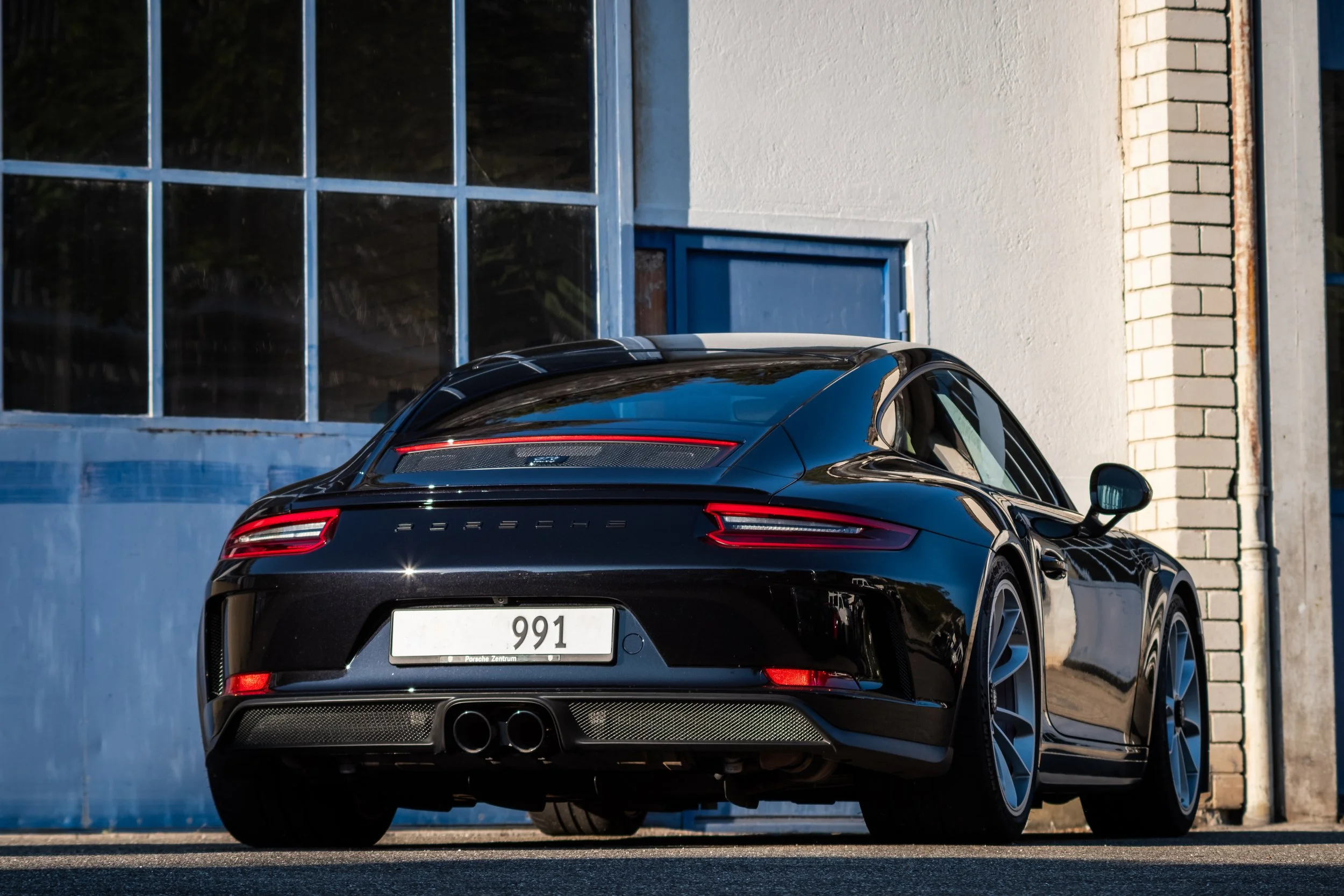 Schwarzer Porsche 911 Sportwagen vor einer weißen Mauer mit blauer Tür wiegt Spiegel und Fenster