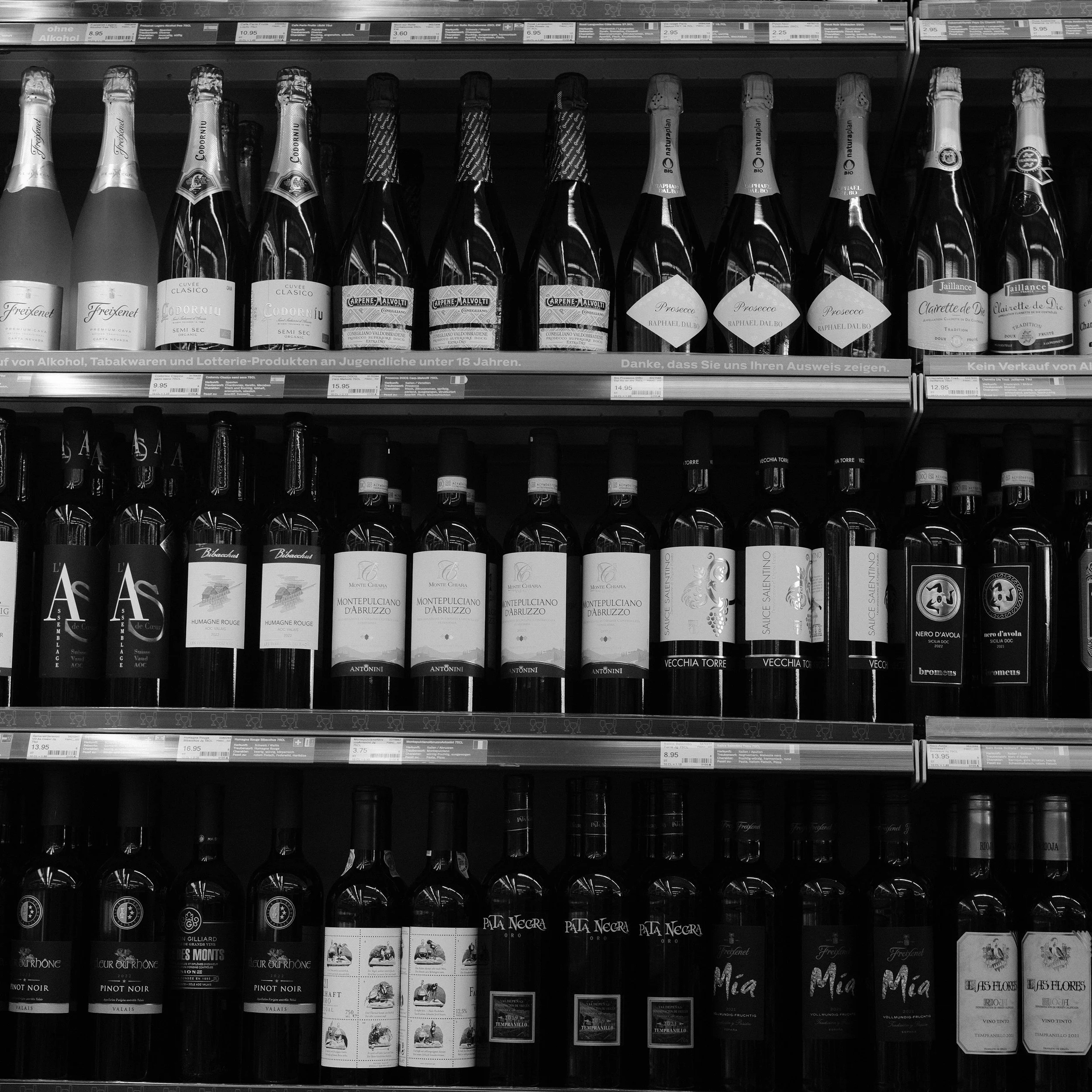 Blick auf mehrere Regale mit Wein- und Sektflaschen in einem Supermarkt.