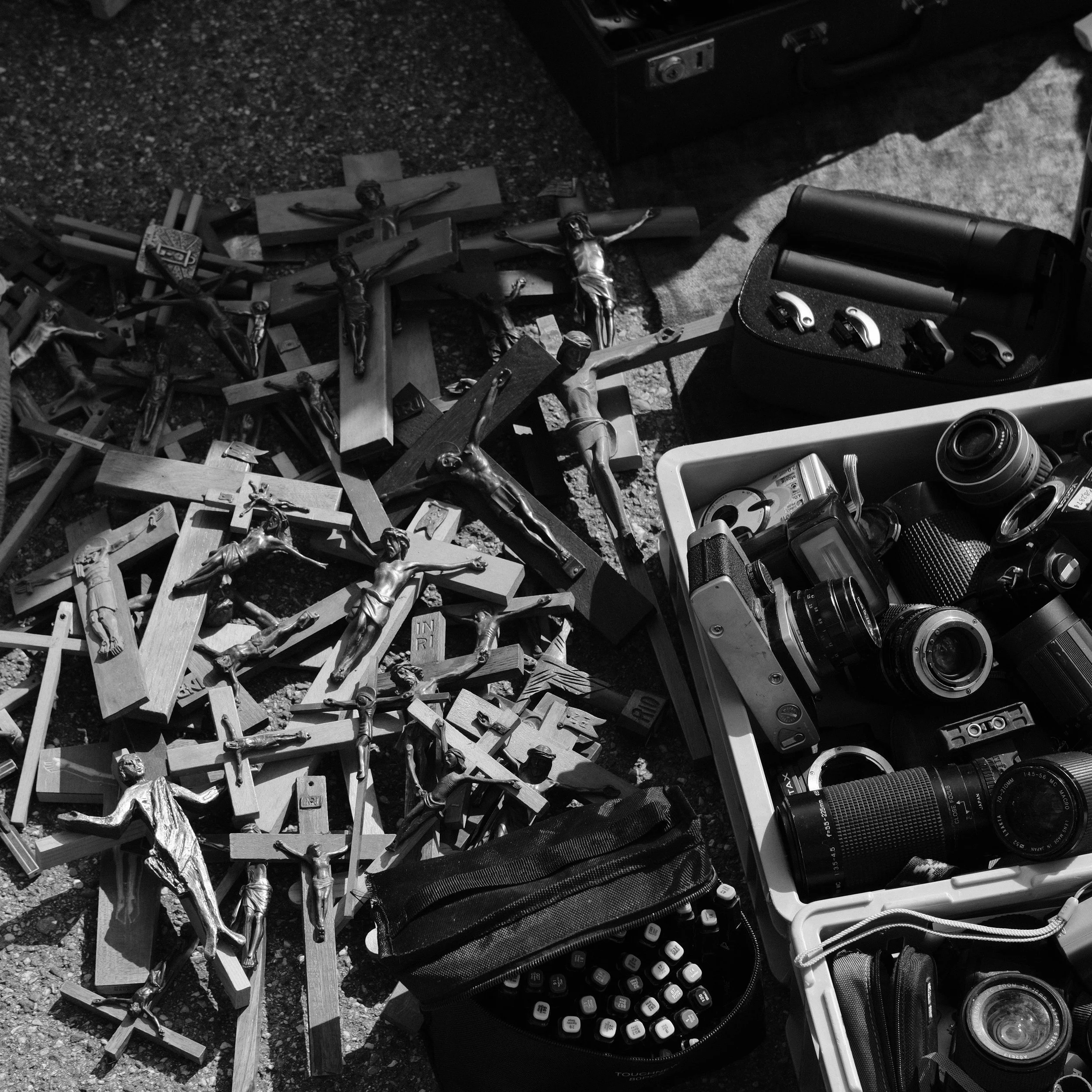 Schwarz-Weiß-Bild mit zahlreichen Jesus-Kreuzen, Kameras, Objektiven und Fotografieausrüstung auf dem Boden.