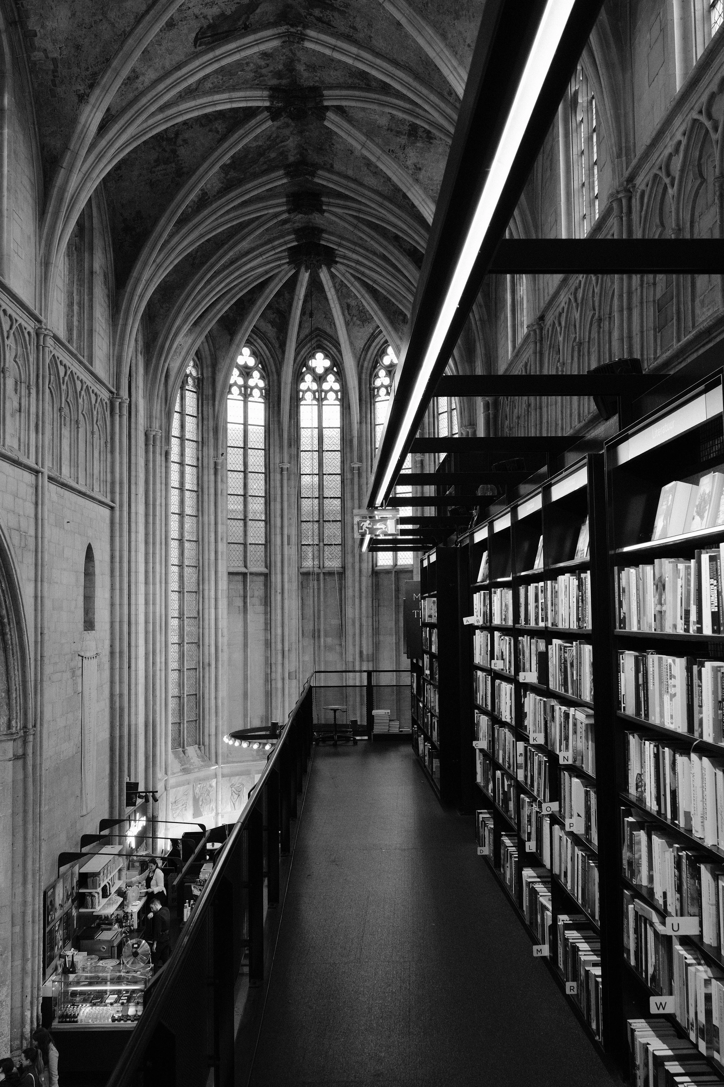 Innenansicht einer gotischen Kirche mit hohen, spitzbogenförmigen Fenstern und Bücherei mit Regalen voller Bücher.