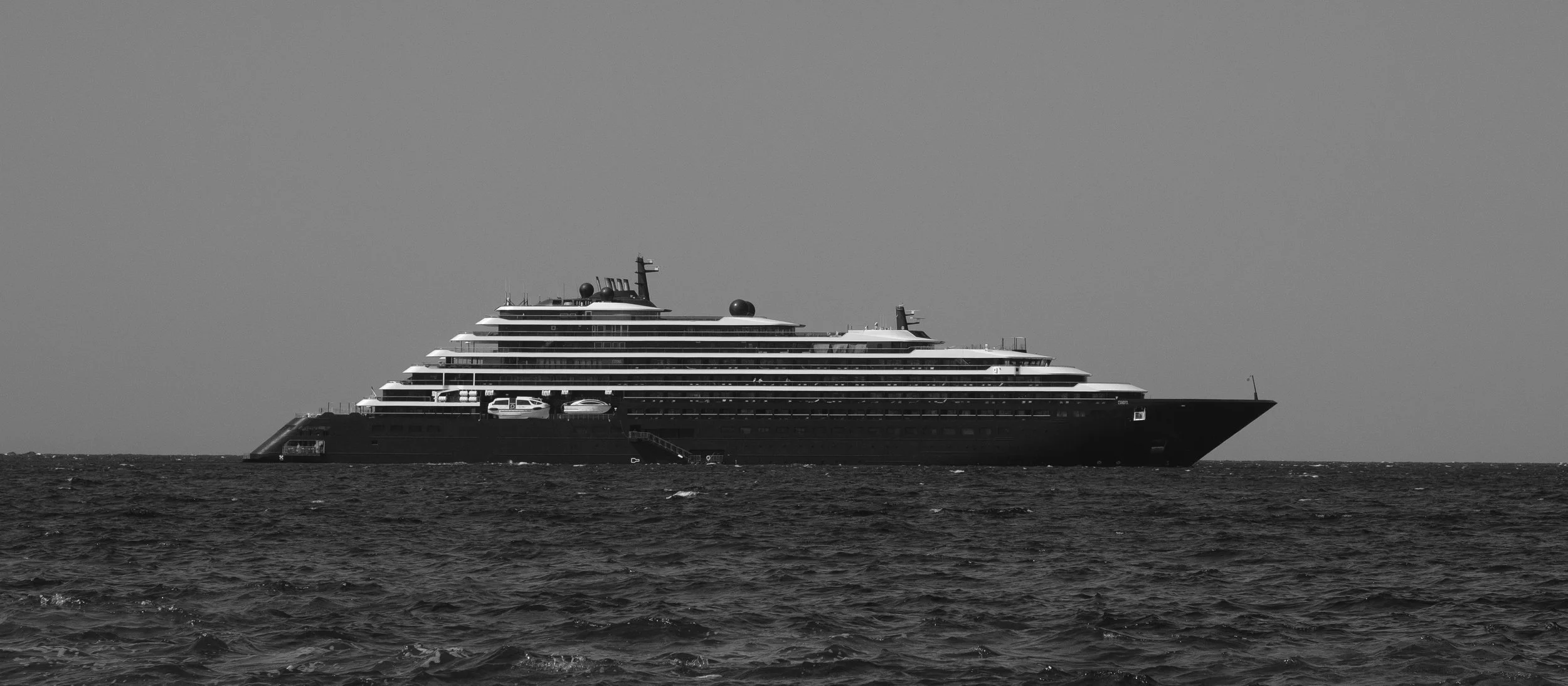 Schwarz-weiß-Foto eines großen Kreuzfahrtschiffes auf dem Meer, Blick seitlich von der Wasseroberfläche bis zum Himmel.