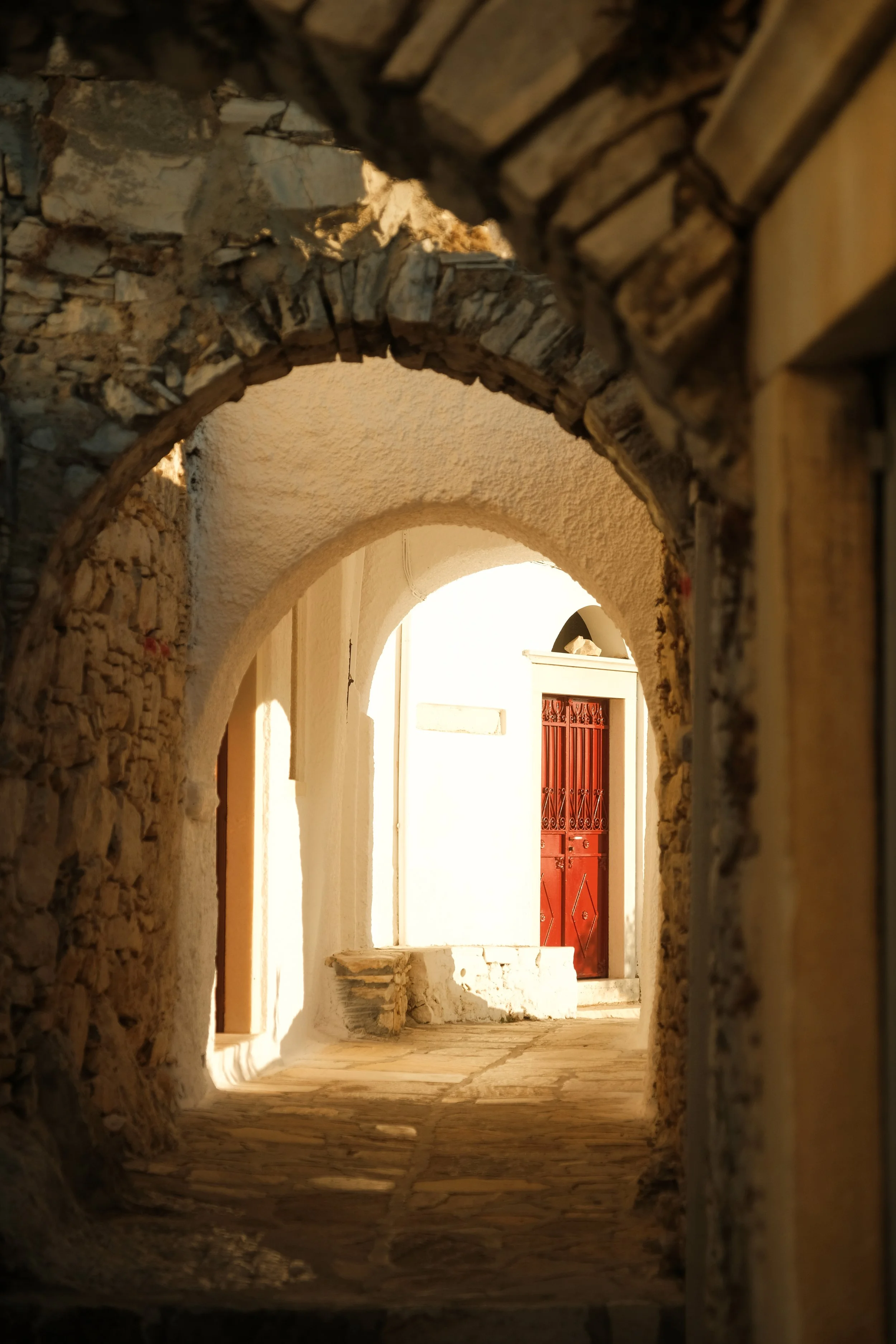 Blick durch eine alte Steinarchitektur auf eine rote Tür im Sonnenlicht.