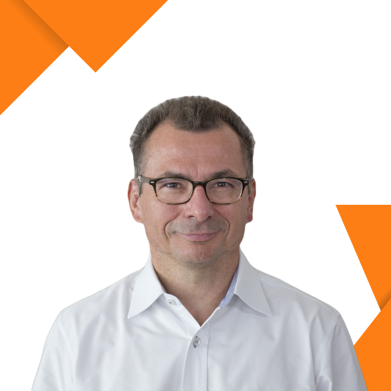 A man with glasses and short dark hair wearing a white dress shirt, smiling against a white background with orange geometric accents.