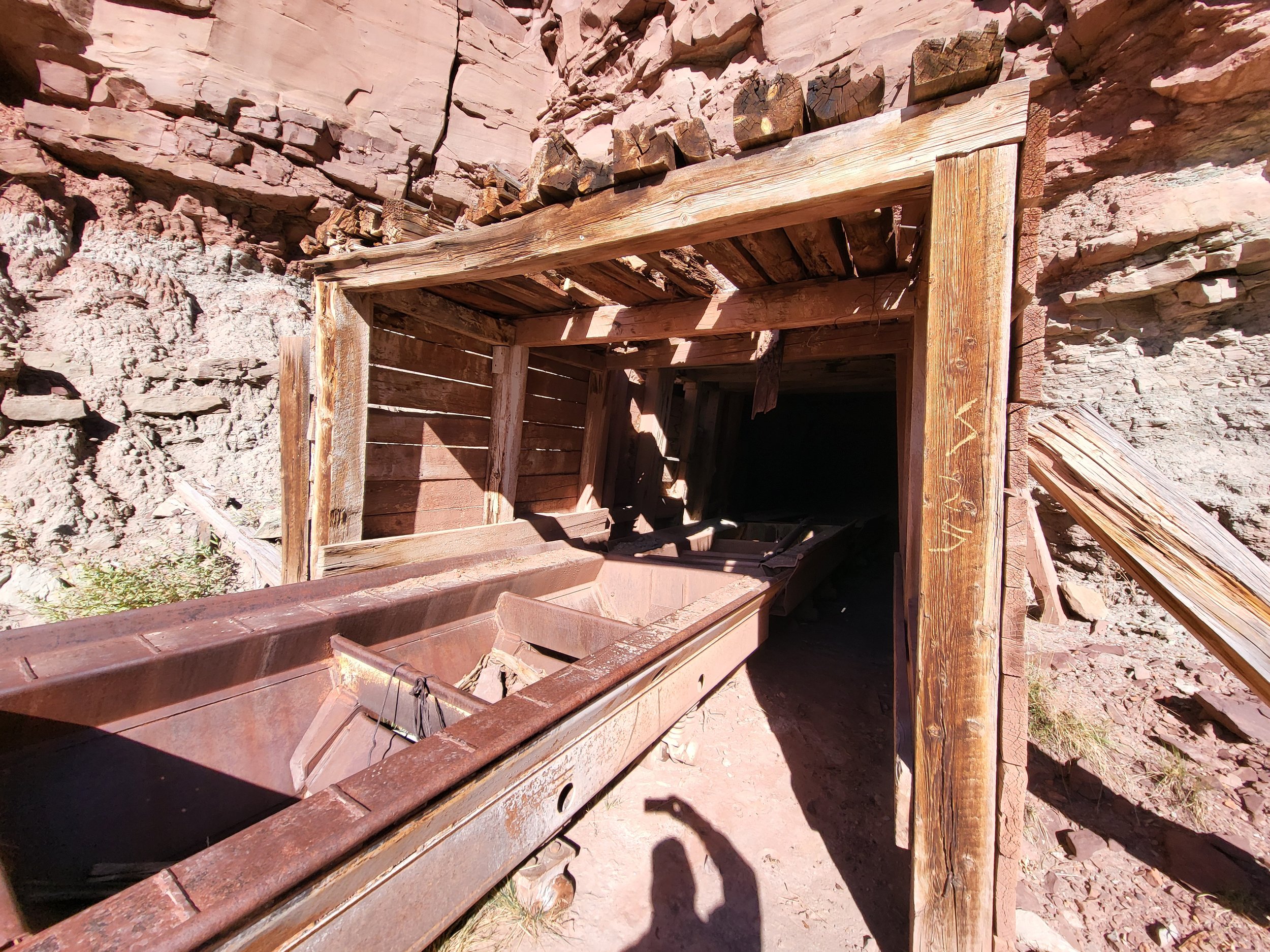 Old wooden mine shaft with a rusted ore cart inside a tunnel carved into a rocky hillside.