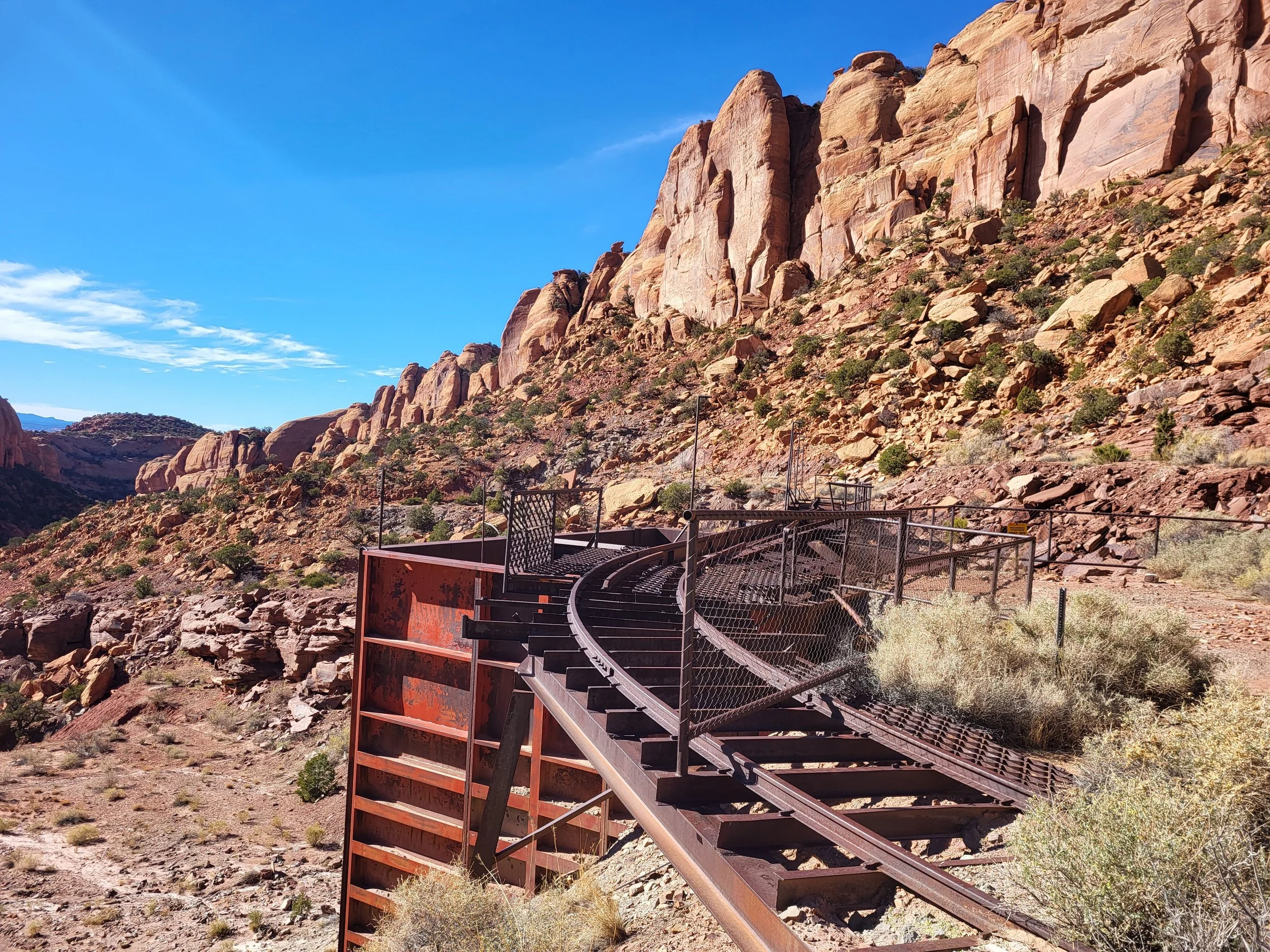 An old abandoned train track with a turntable in a desert landscape with rocky hills and a clear blue sky.