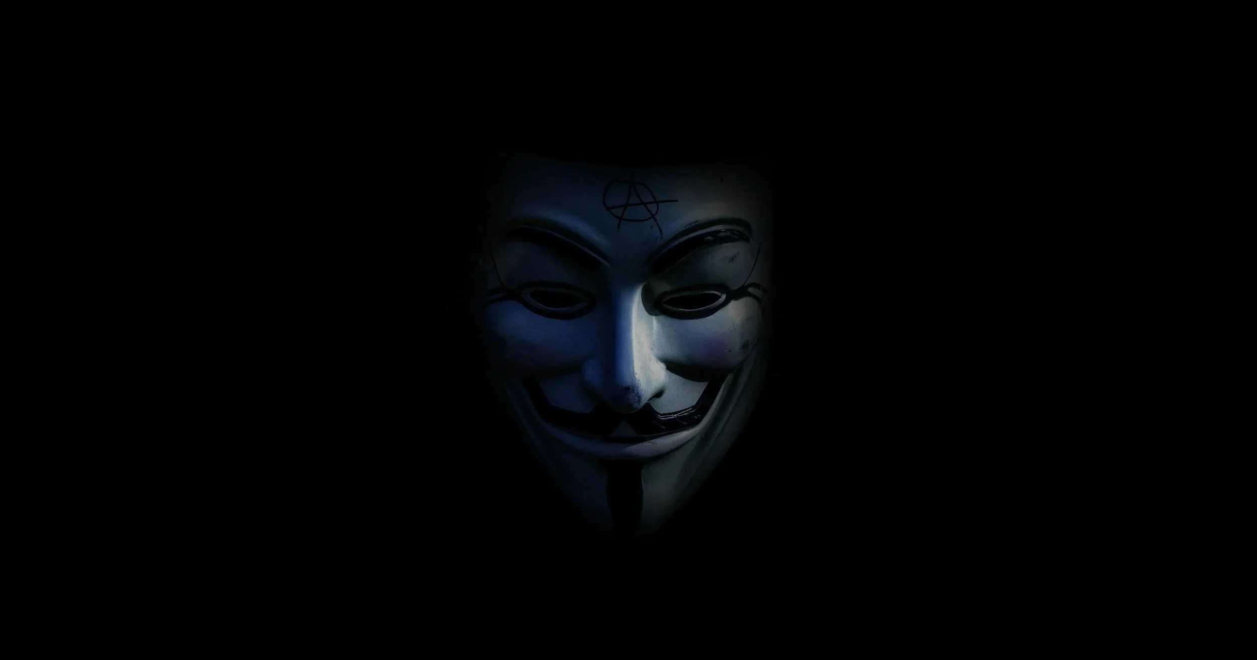 A Guy Fawkes mask illuminated in darkness, symbolizing anonymity or rebellion.