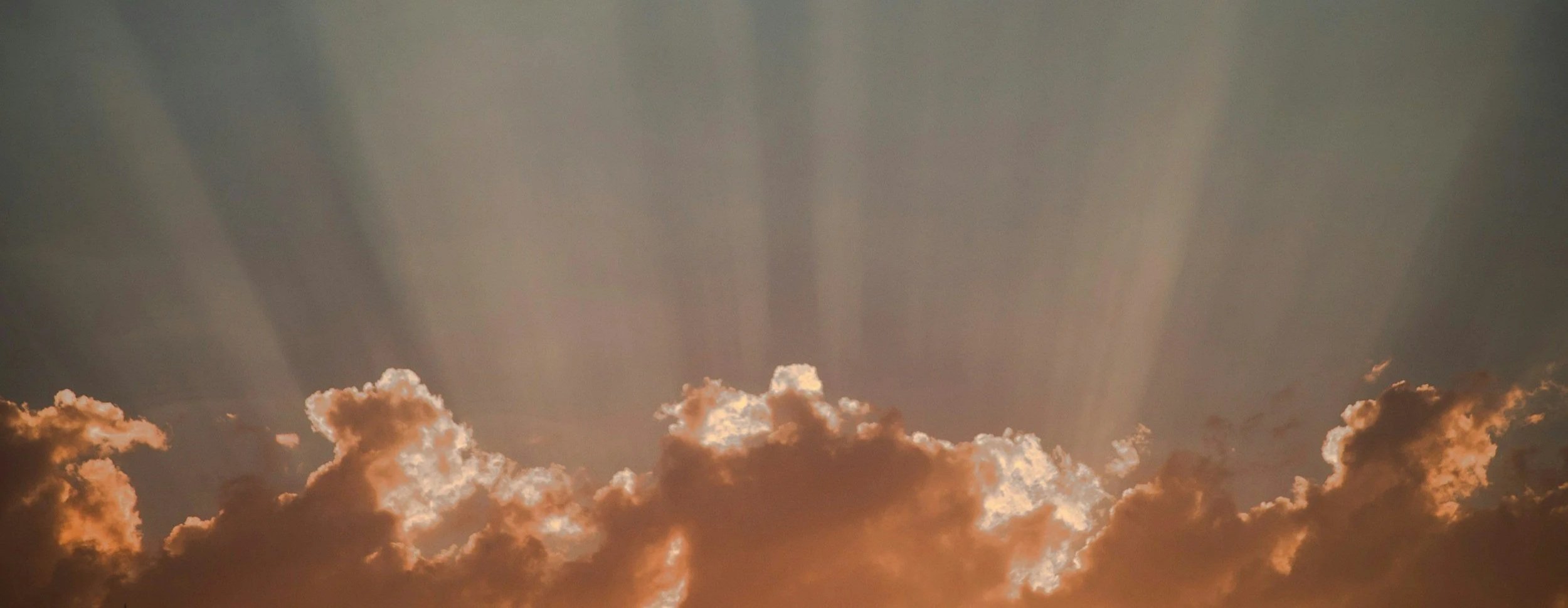 Sun rays shining through clouds in the sky during sunset or sunrise.