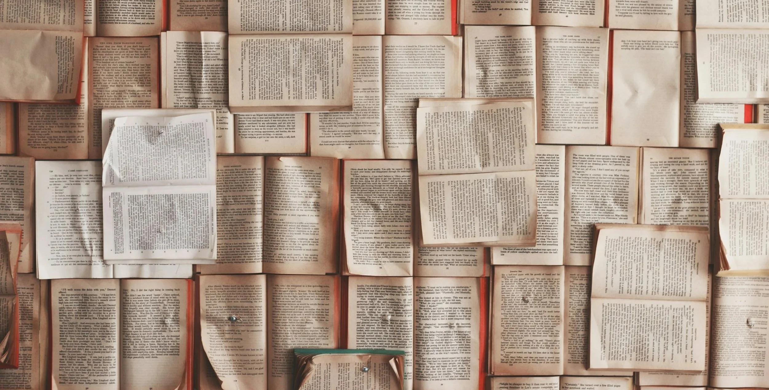 A collage of open books arranged with some pages crumpled or folded, displaying various texts on cream and white pages.