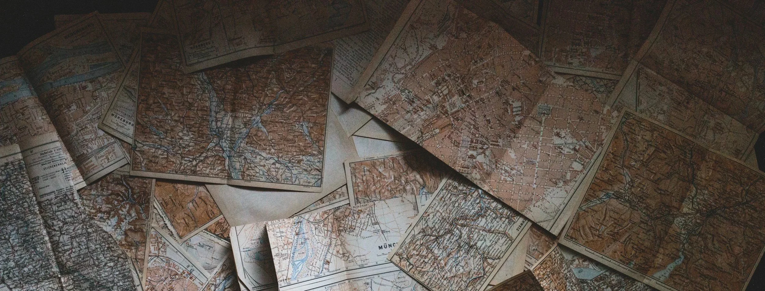 Several vintage maps spread out and overlapping each other, showing terrain, streets, and waterways.