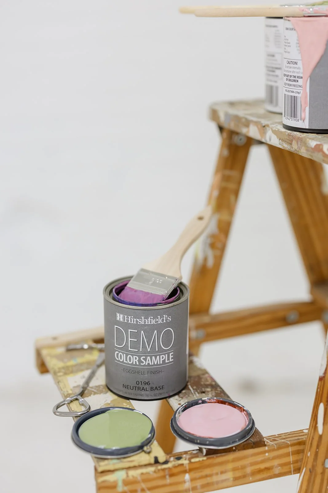 Open paint can with pink and green paint swatches on a wooden ladder, representing professional painting contractors in Minneapolis.