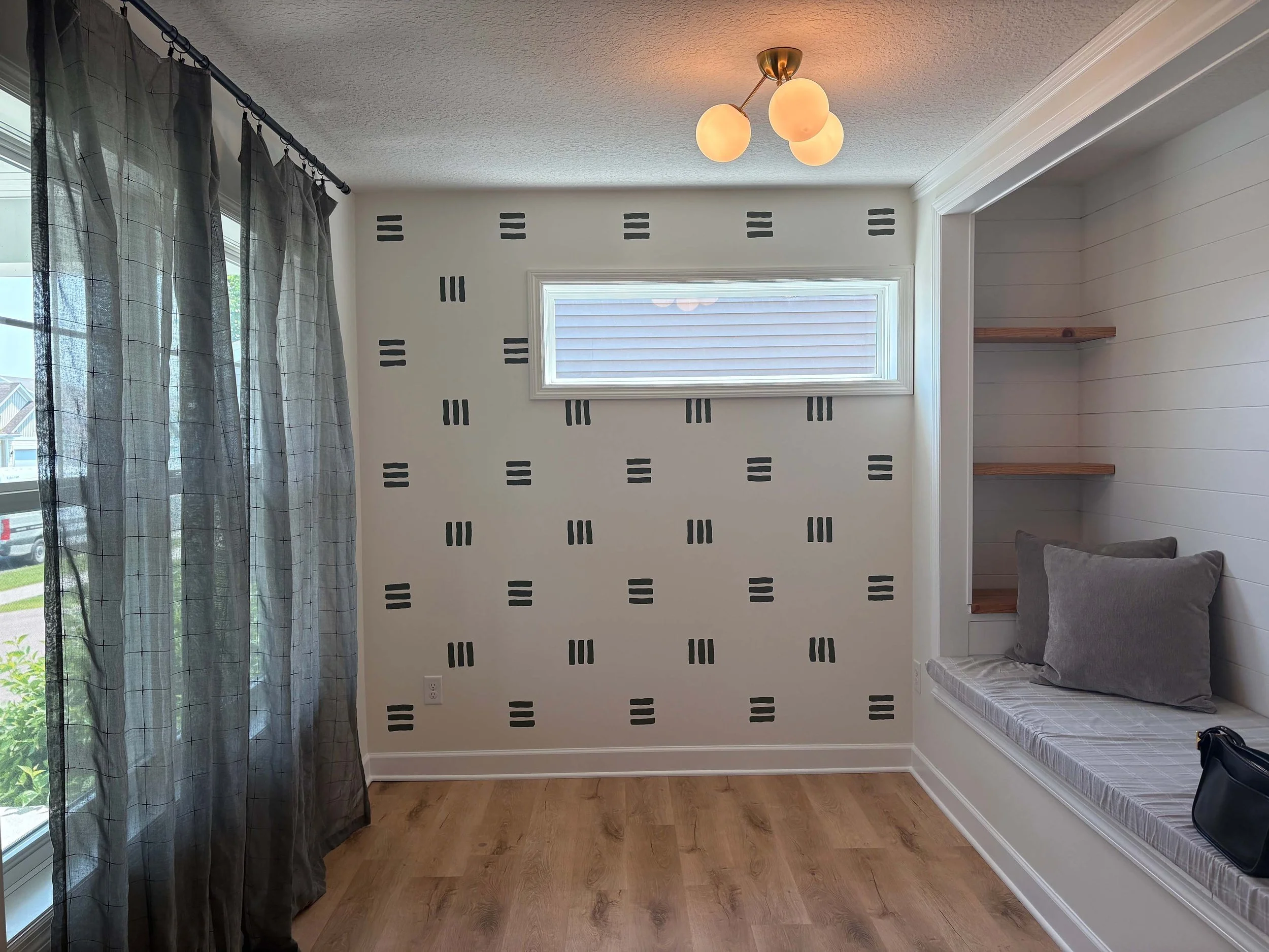 A modern bedroom featuring a custom patterned accent wall and built-in window seat, highlighting specialty interior painting in MN.