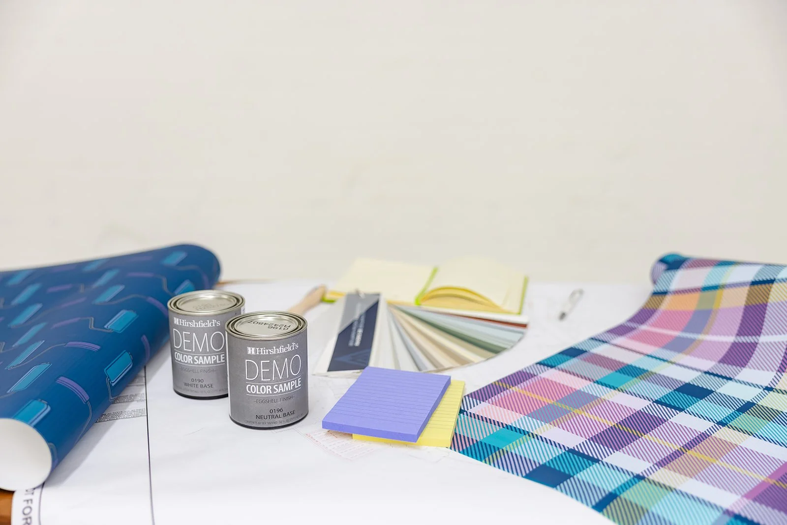 A flat lay of interior design and painting supplies, including paint color samples, cans of paint, fabric swatches, and a color palette on a white surface.