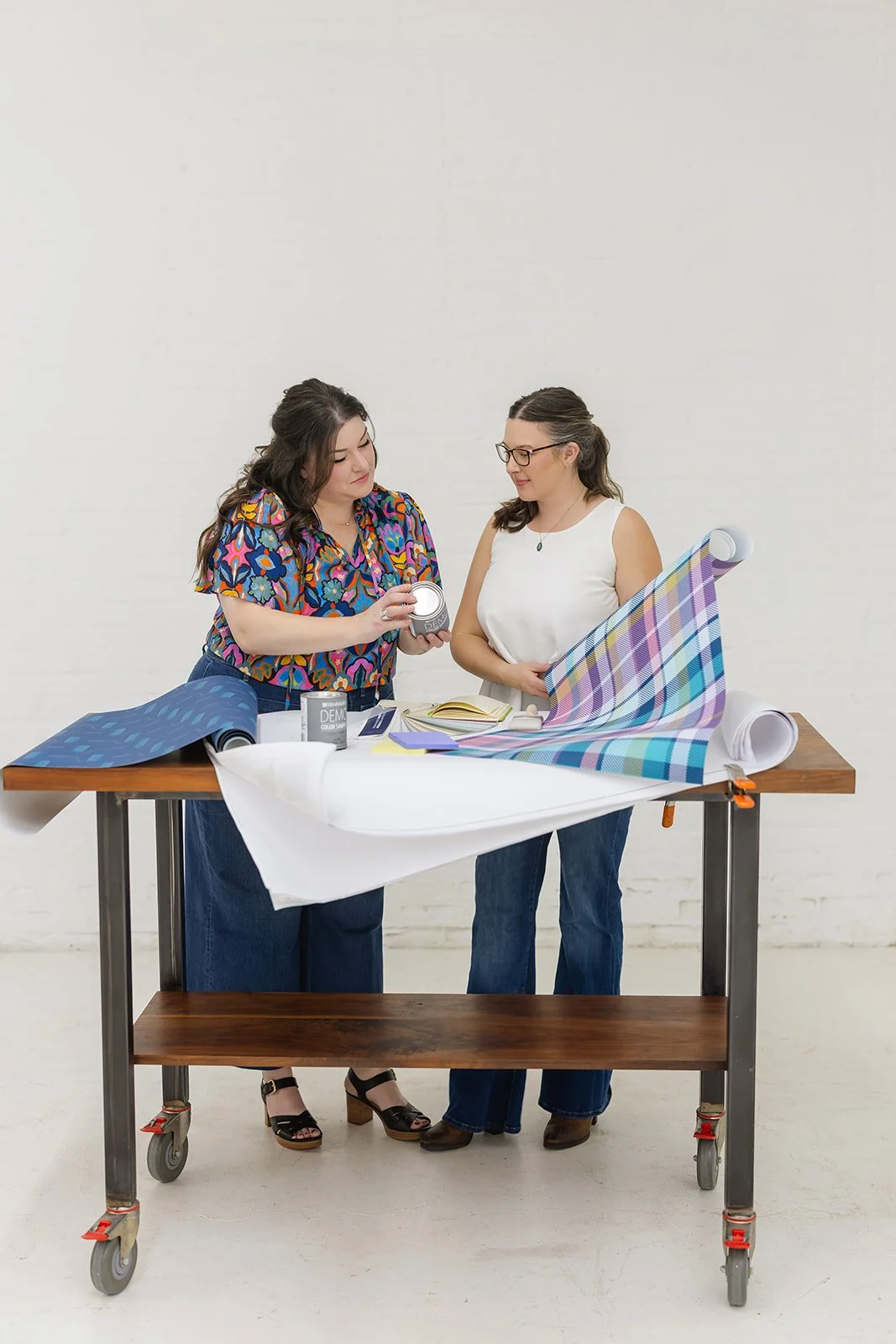 The founders of The List, professional house painters in Minneapolis, reviewing wallpaper samples and color swatches at a workbench.