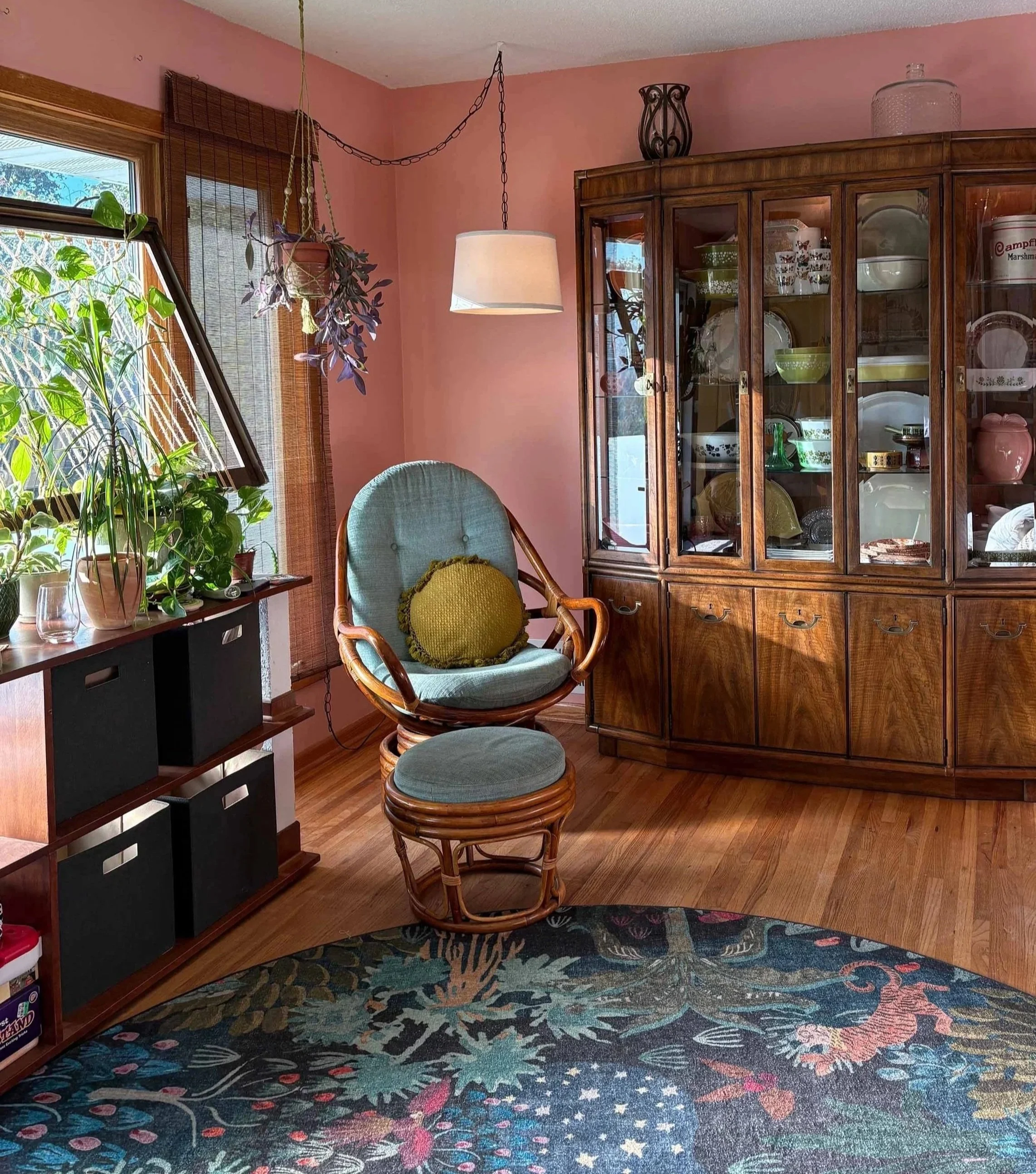 Warm pink painted living room featuring a vintage wooden hutch and cozy teal armchair styled by The List in Minneapolis.