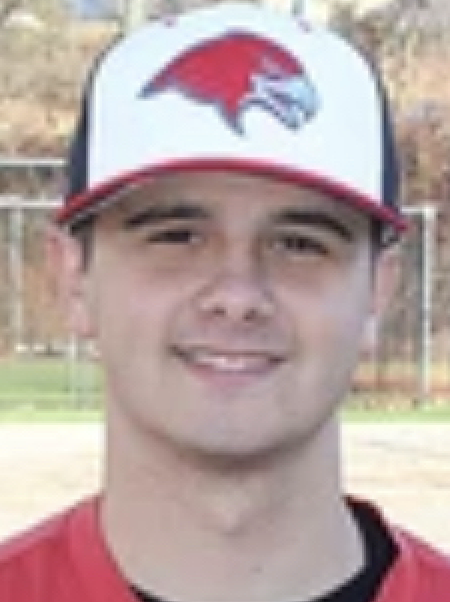 Young man smiling, wearing a red and white baseball cap with a bird logo, outdoors on a sports field.