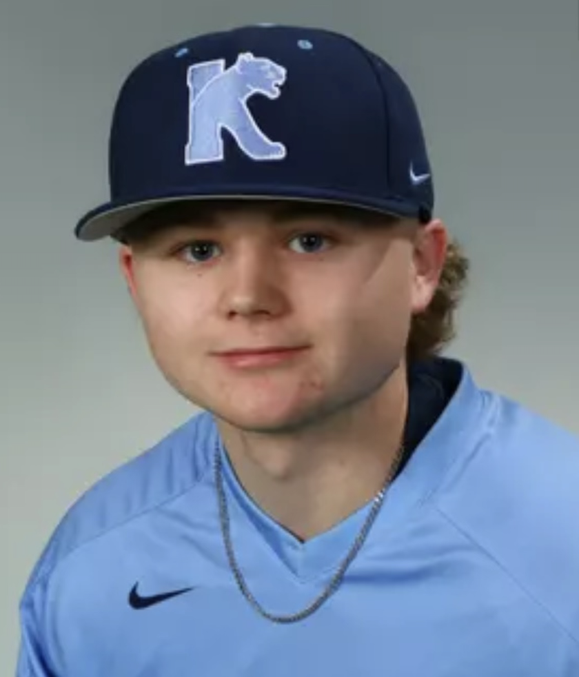 Young man wearing a blue sports jersey, a black cap with a bear logo, and a silver chain necklace.