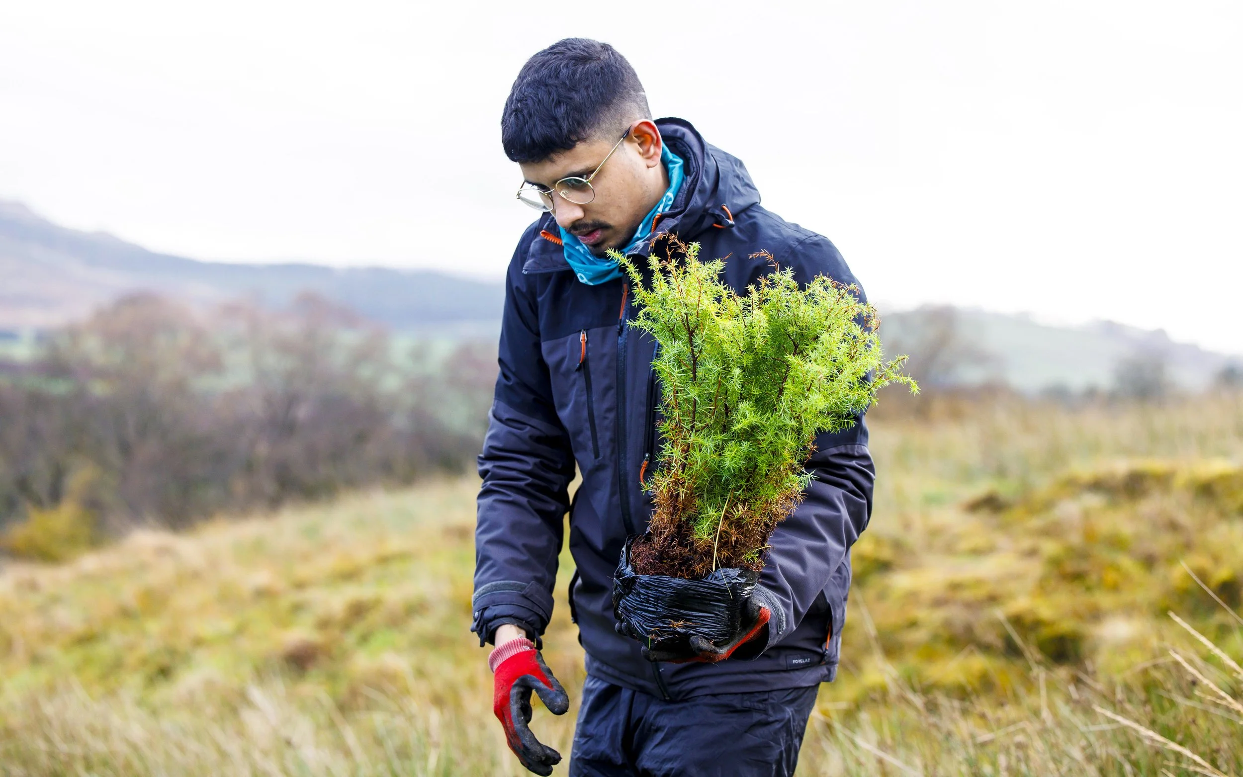 Three people sitting outdoors in a grassy area, engaging in a conversation, with trees and a house in the background.