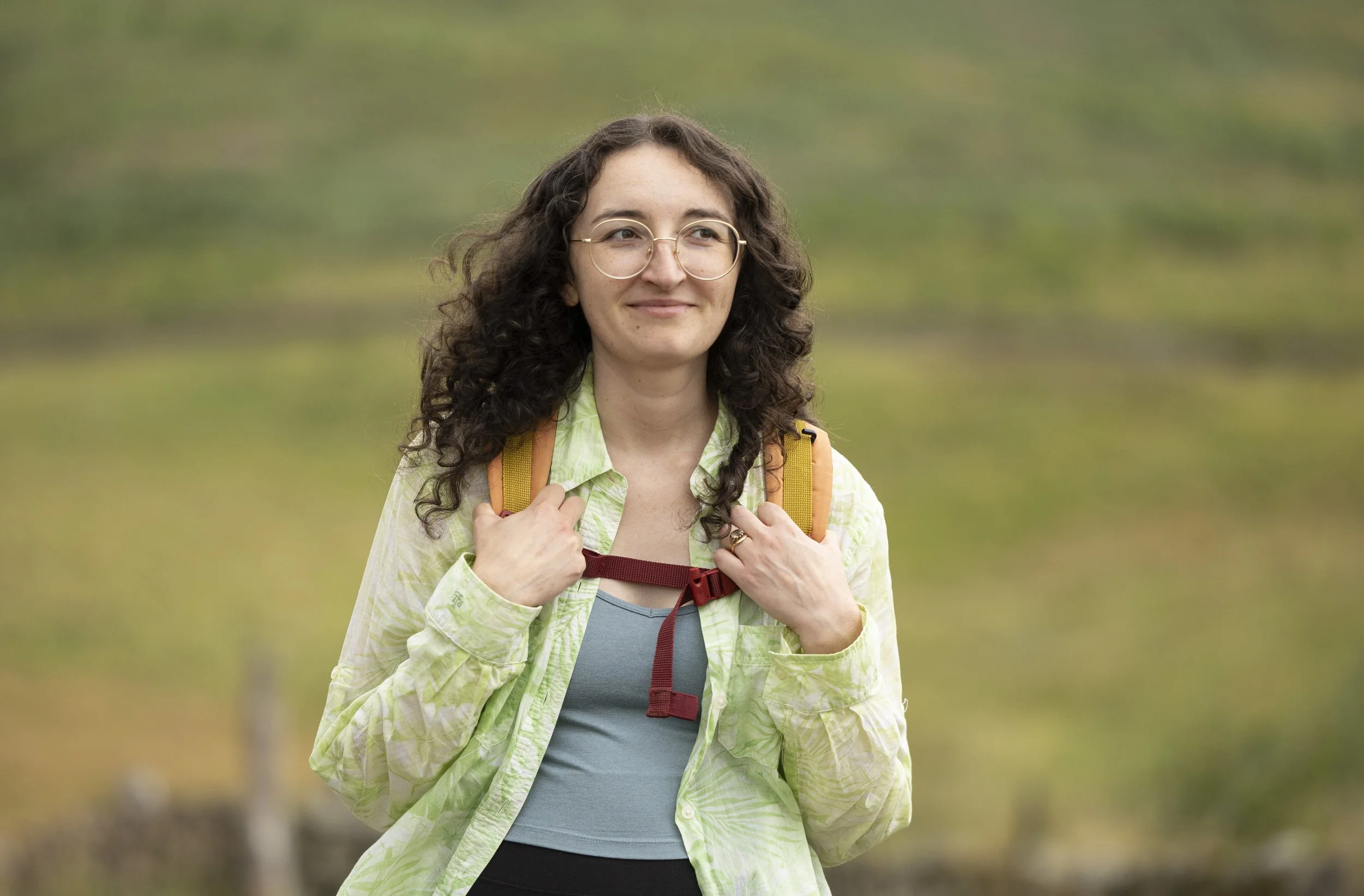 A young lady walking towards the camera in the countryside with a rucksack on and smiling.