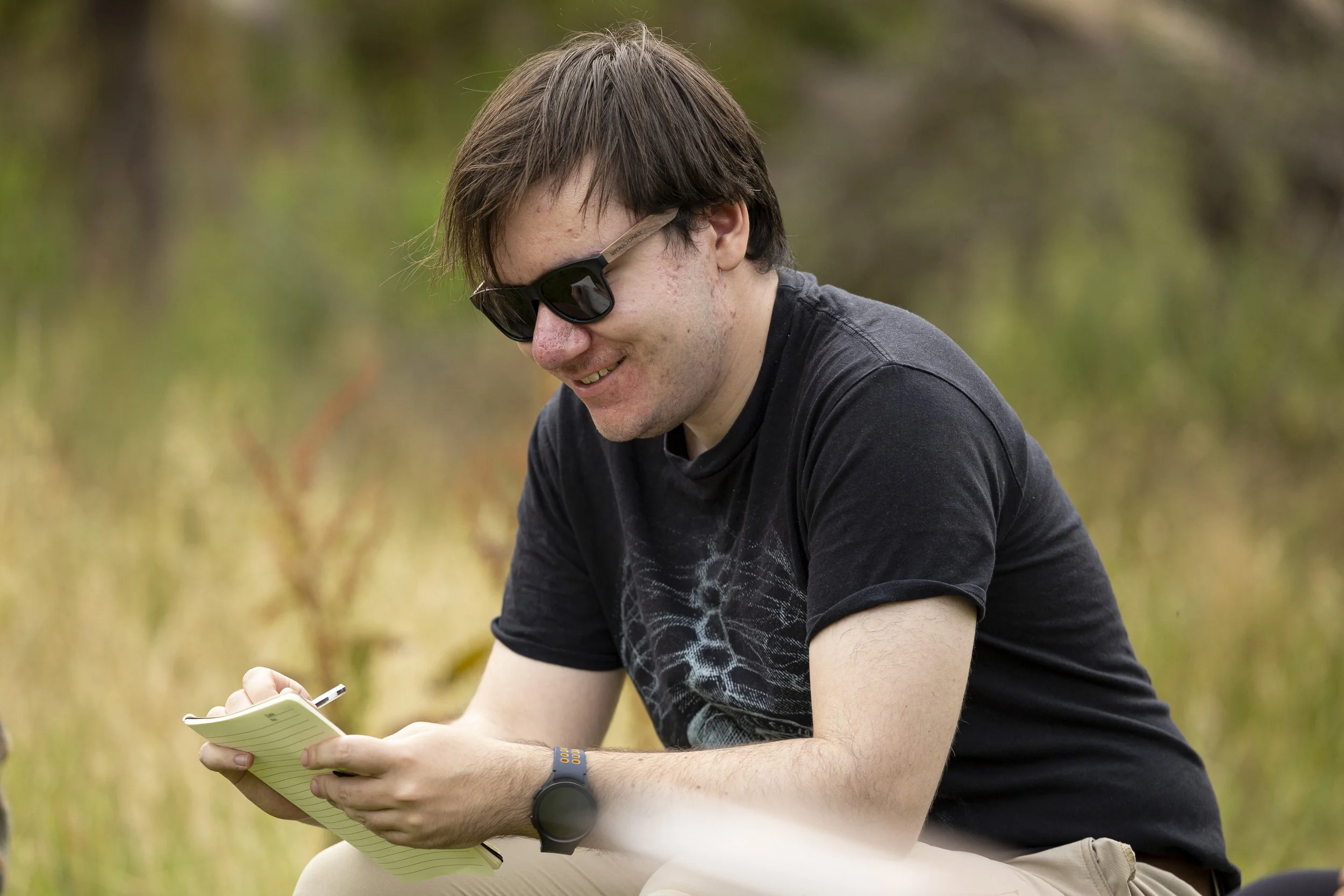 A young man sitting int he countryside reading a book.