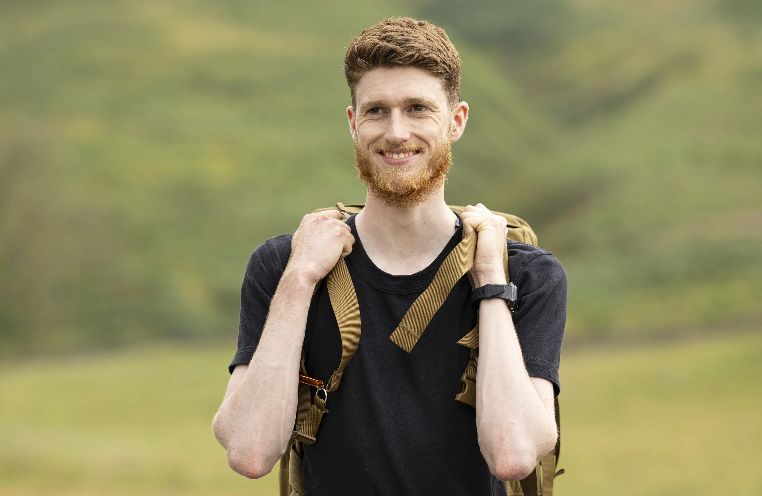 A young man looking into the distance smiling in the countryside with a rucksack on.