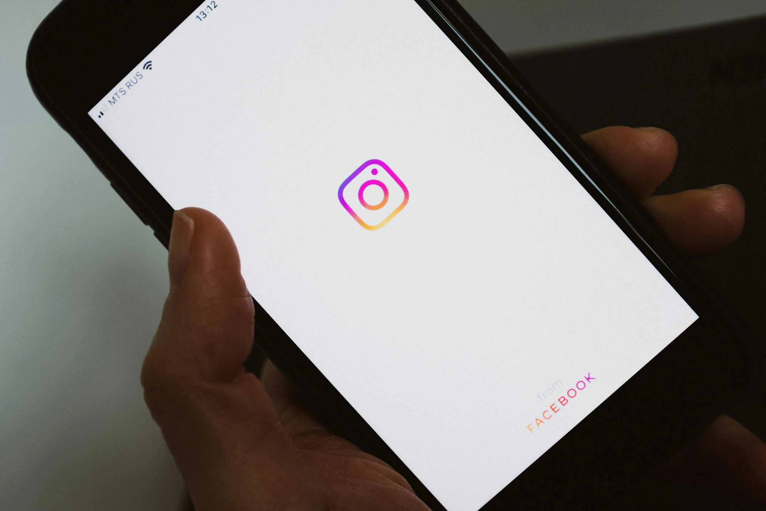 Hand hält Smartphone mit Instagram-Logo auf weißem Hintergrund.
