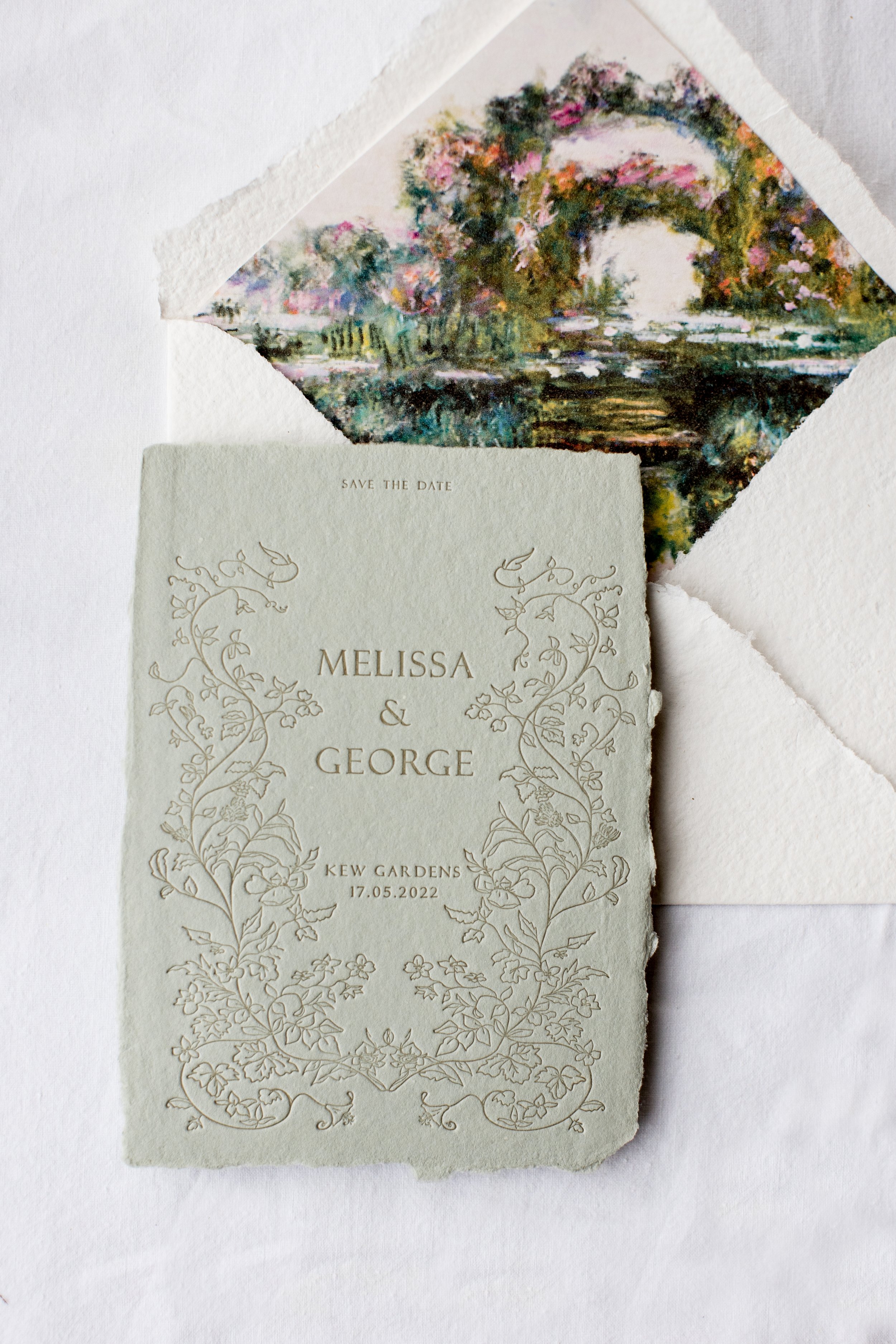 Wedding invitation with floral design and a save the date message, placed on white background, with a colorful watercolor painting of a landscape with trees and a river in the background.
