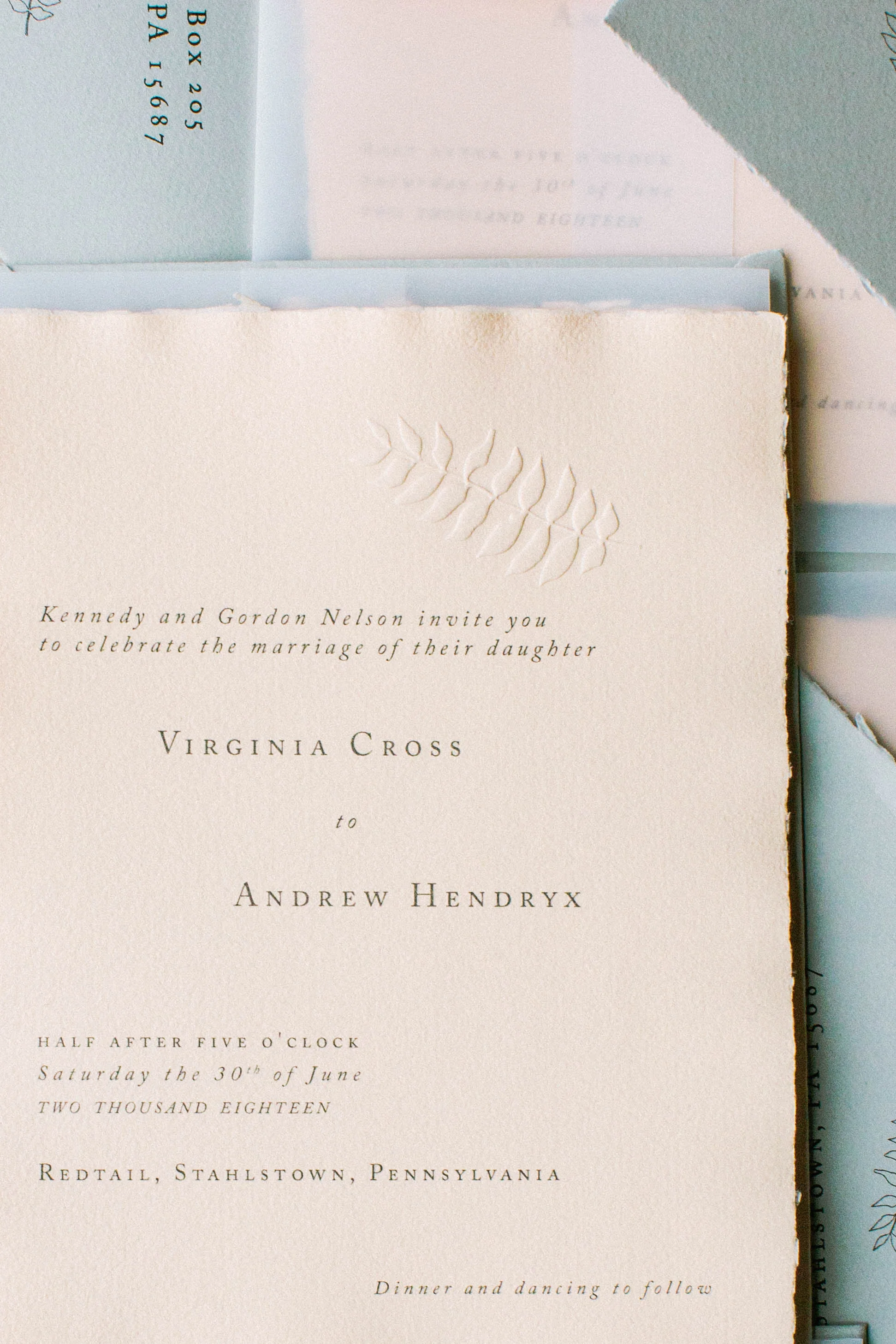 A wedding invitation card with embossed leaf detail at the top, printed with elegant black text on cream-colored paper.