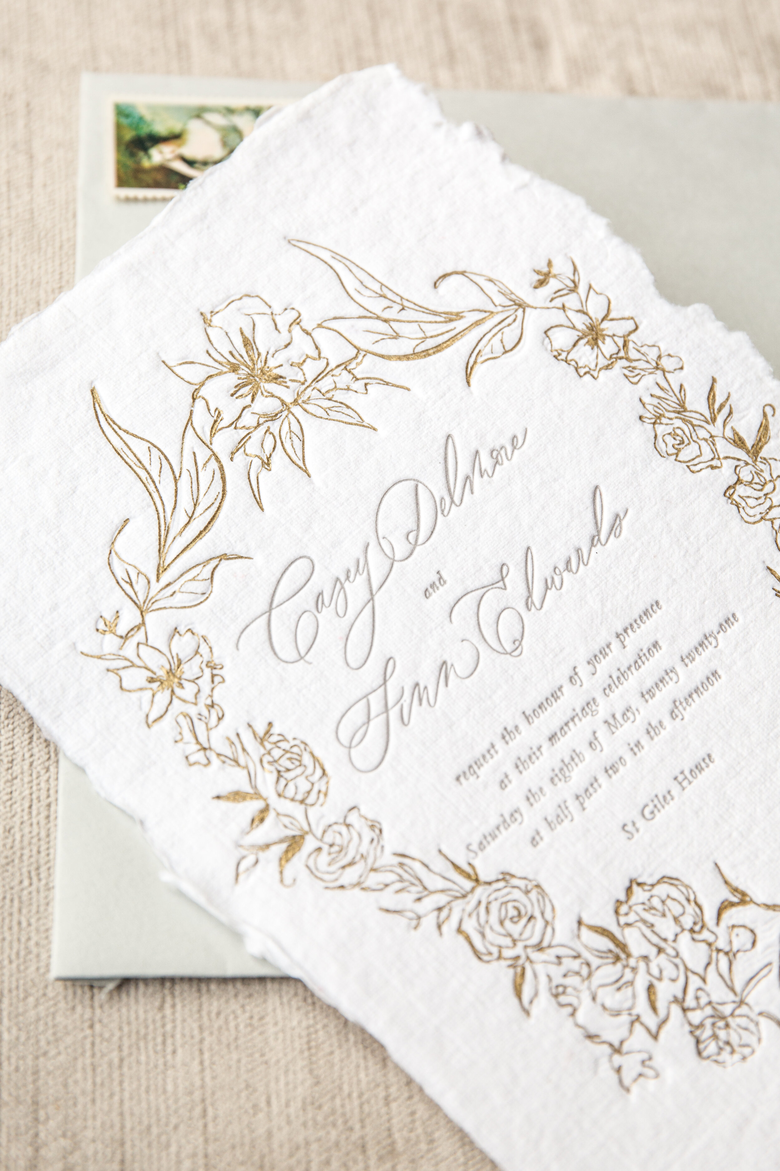 Letterpress and foil wedding invitation with gold floral border and elegant cursive text on textured white paper.