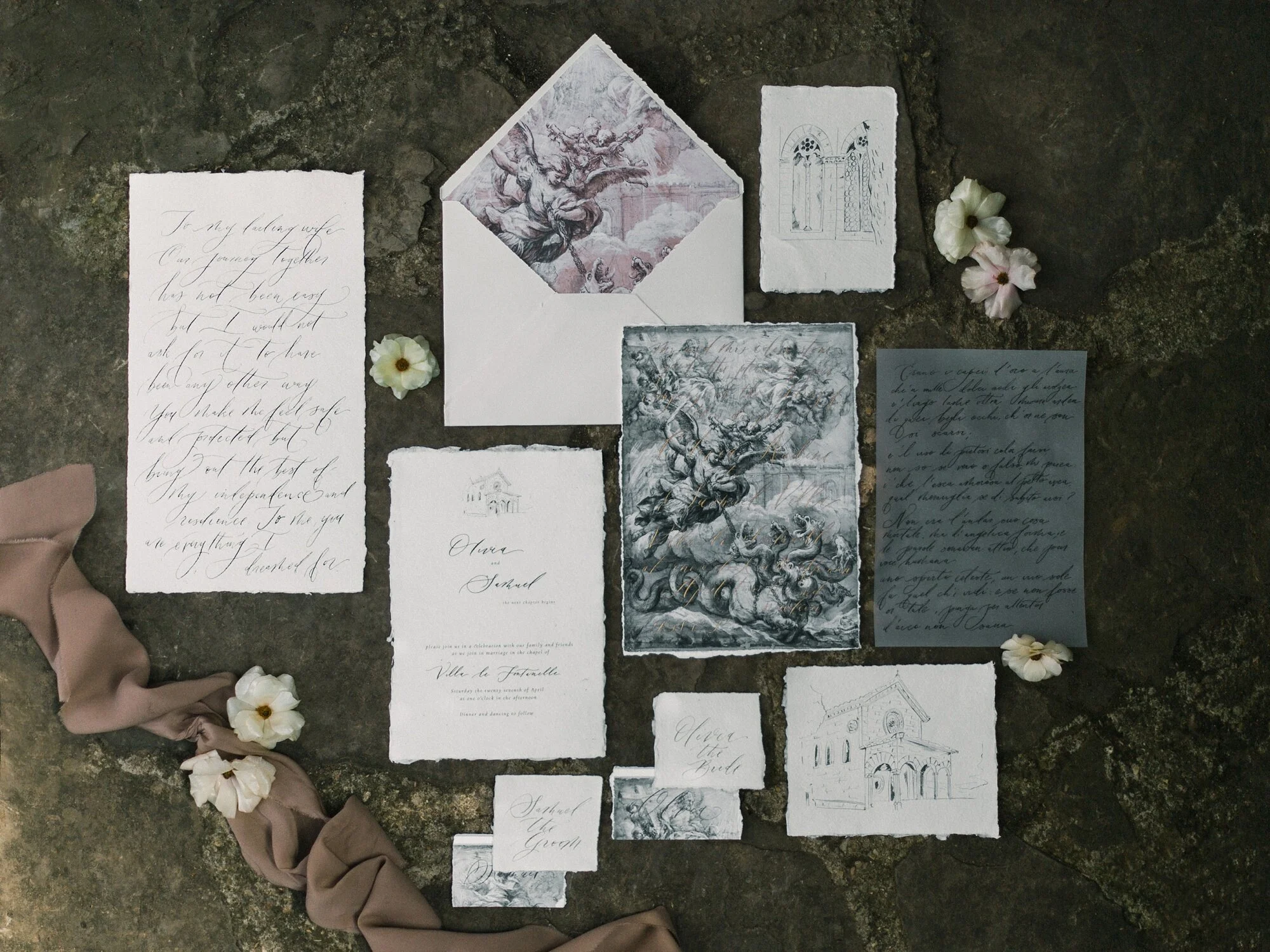 Collection of handwritten and printed wedding stationery, including invitations, notes, and cards, arranged on a dark textured surface with white flowers and beige fabric.