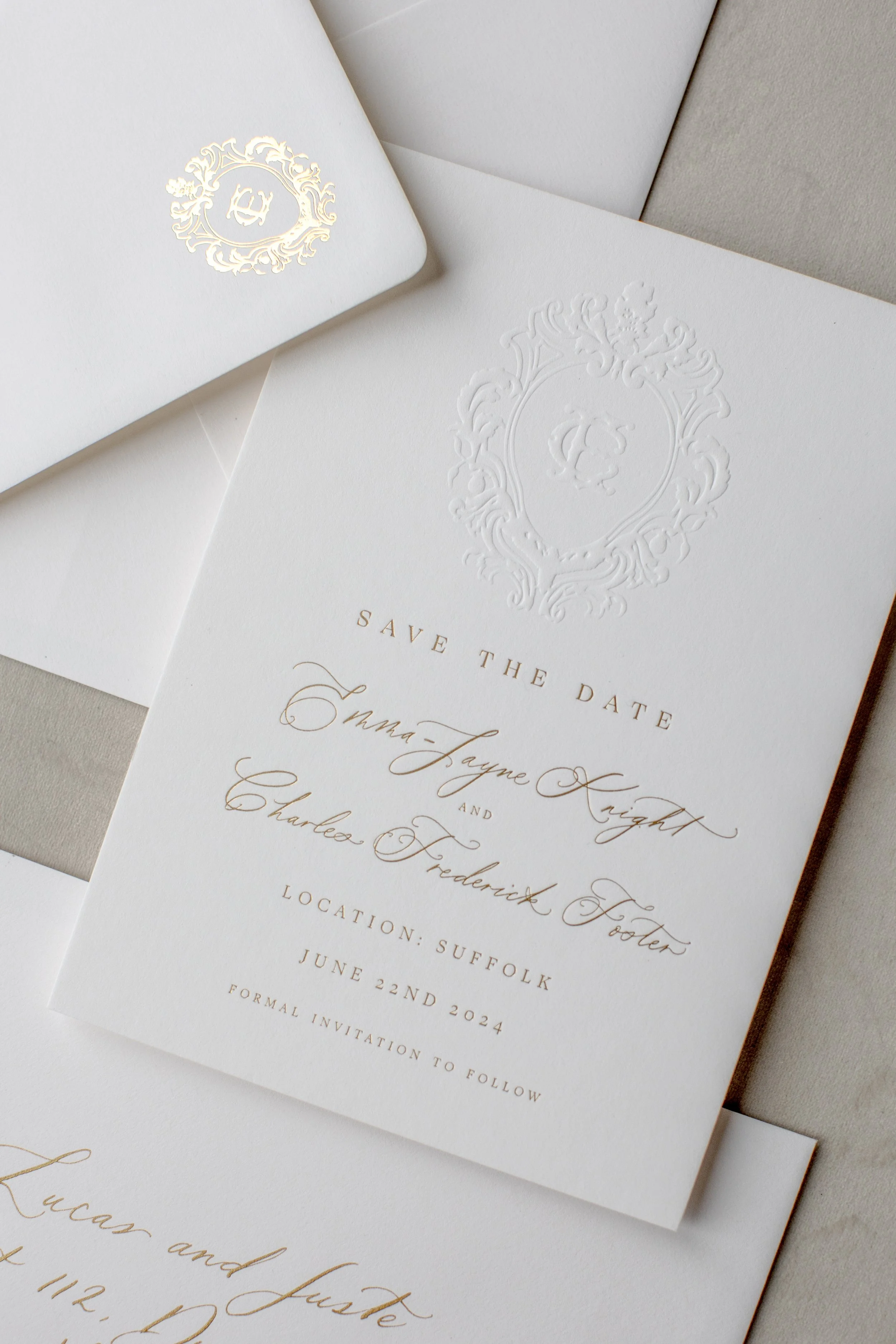 Elegant wedding save the date card with embossed crest and gold lettering, surrounded by matching envelopes.