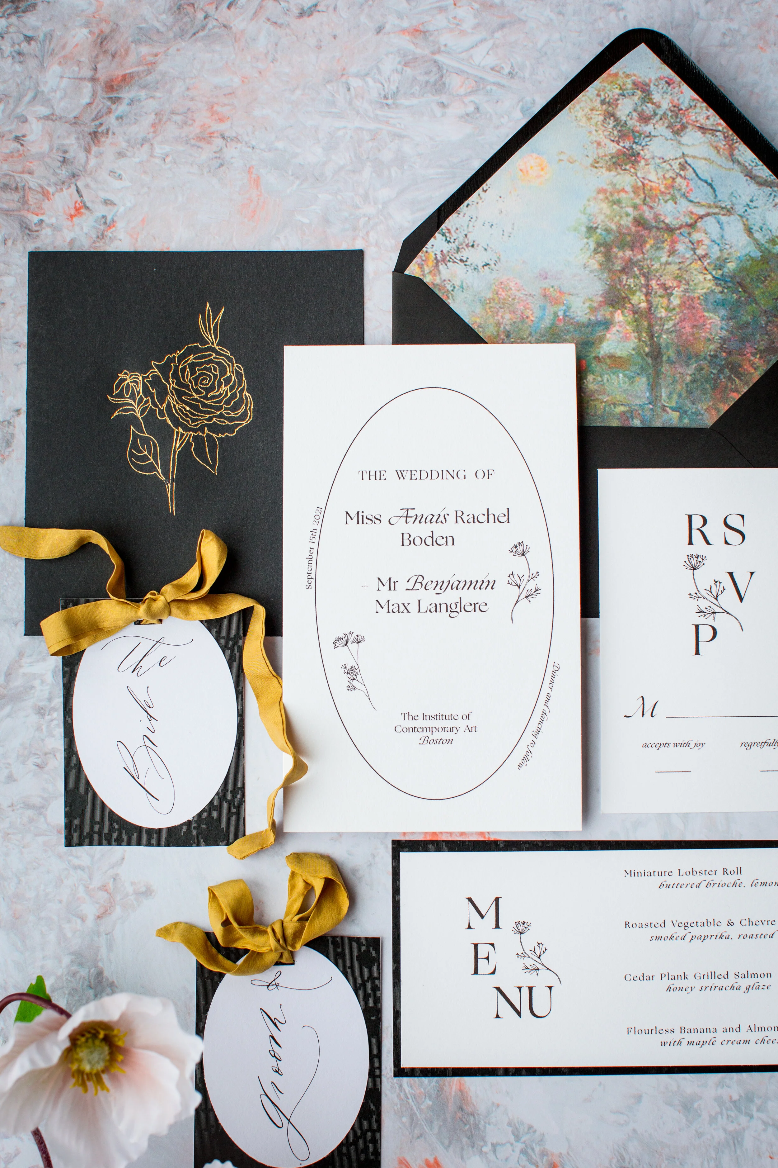 Wedding invitations and accessories, including a menu, save-the-date card, and tags, displayed on a marble surface, with floral and landscape elements.