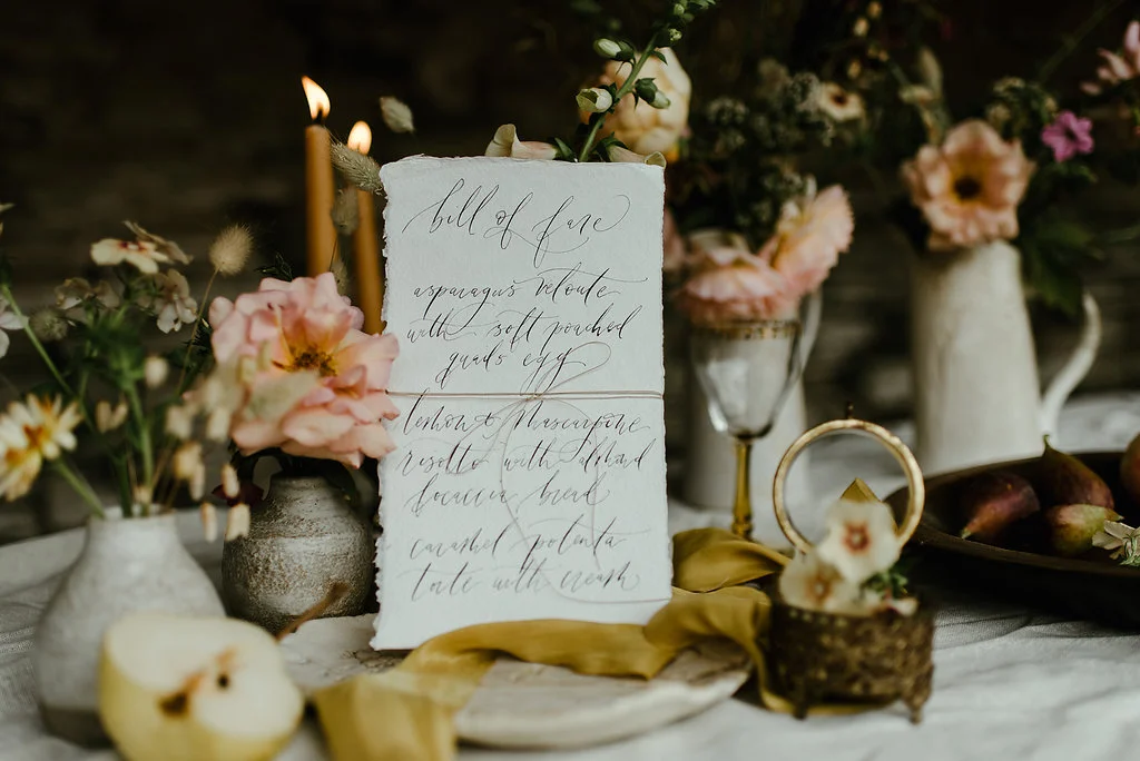 A decorated table with flowers, candles, and handwritten menu cards for a special event or celebration.