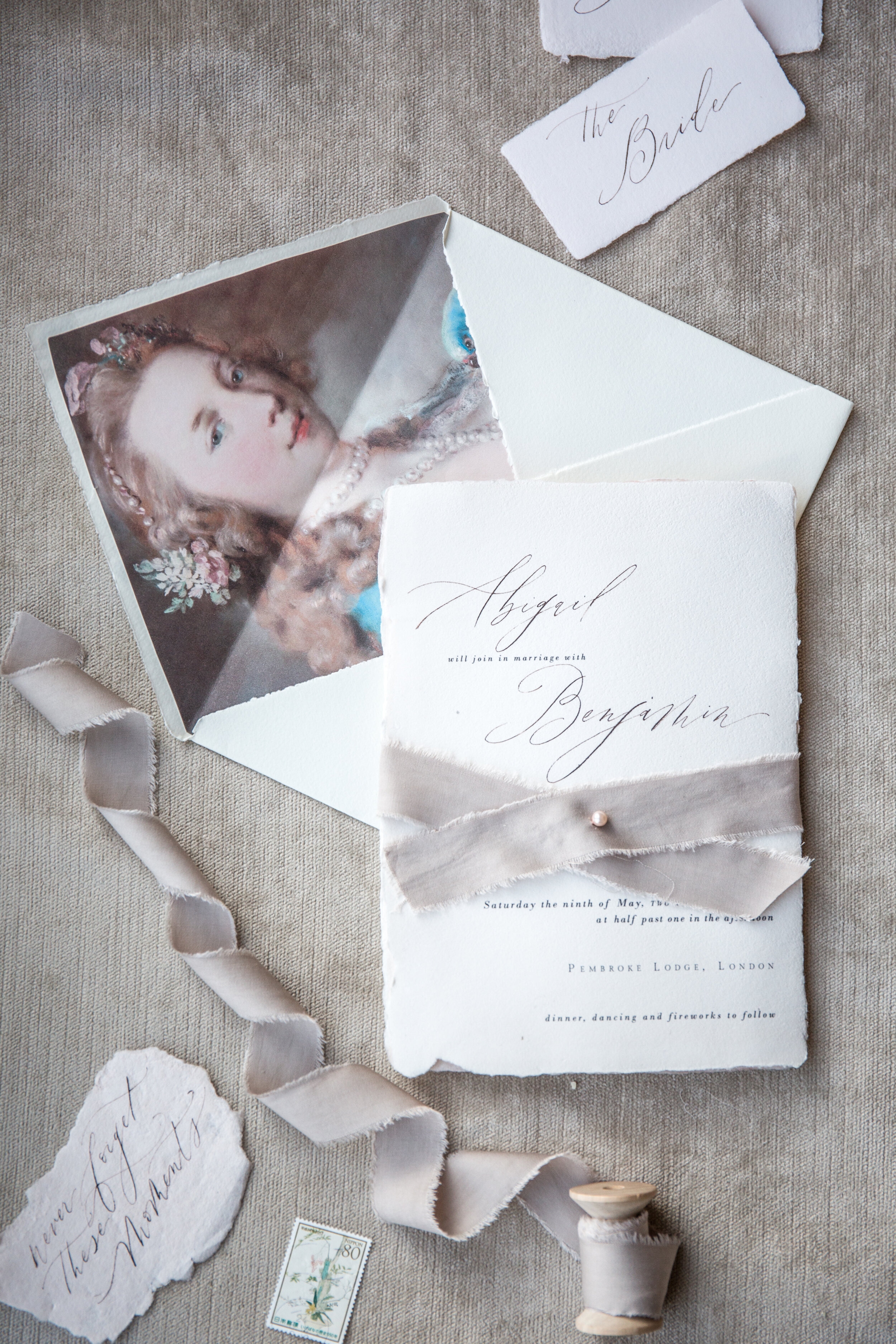 A wedding invitation set with a portrait of a young girl, handwritten notes, and a postage stamp on a textured surface.