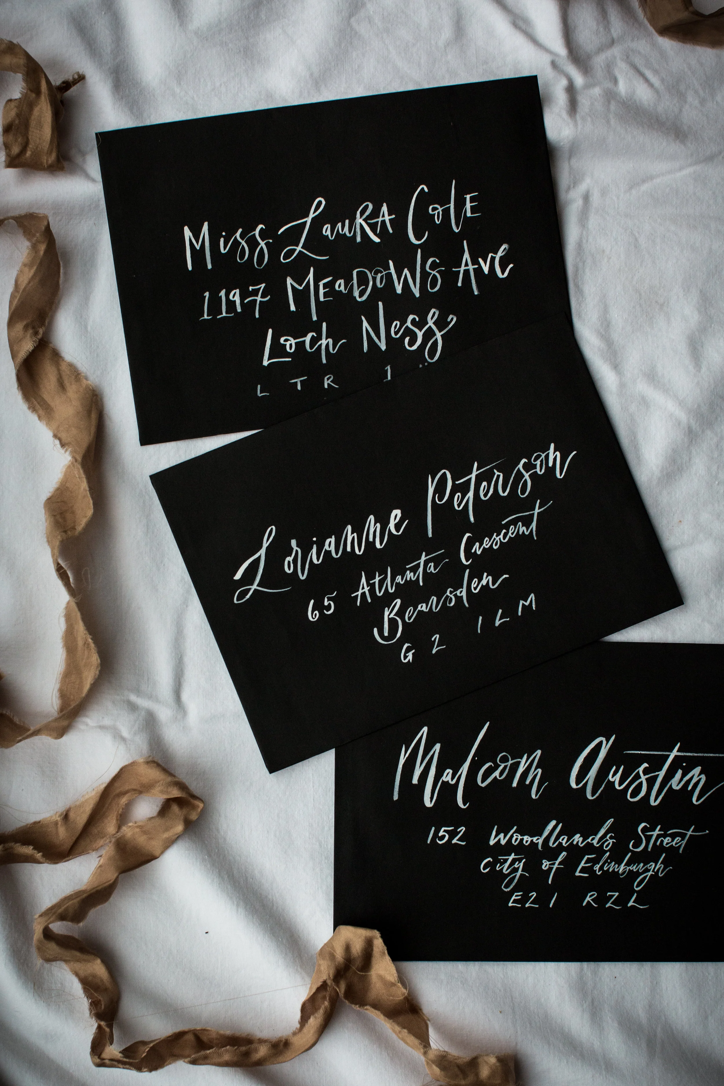 Black hand-lettered address cards on white fabric, with torn brown paper strips around them.