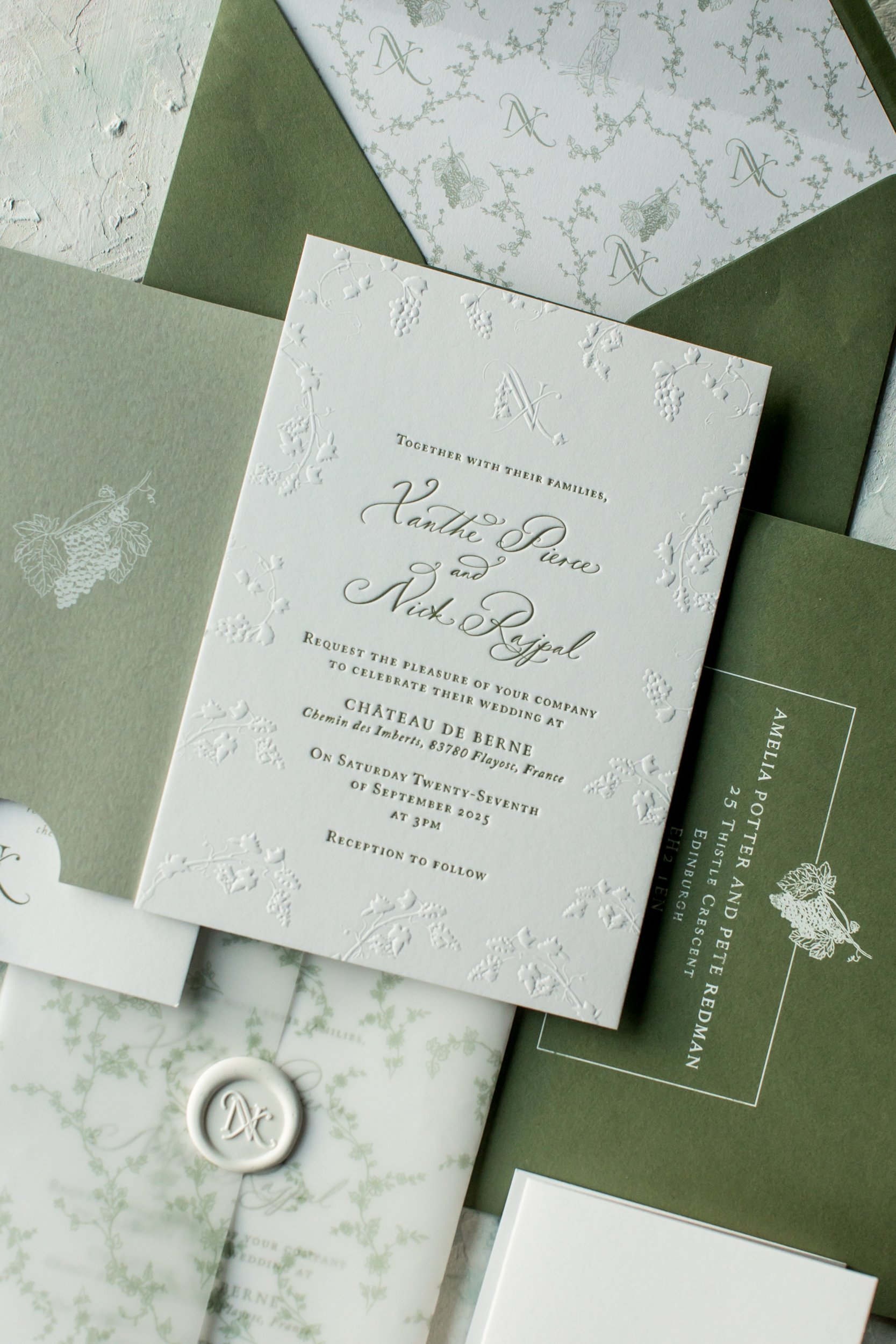 Elegant wedding invitation with embossed floral details, surrounded by matching stationery in shades of green and white, including an envelope with a wax seal.