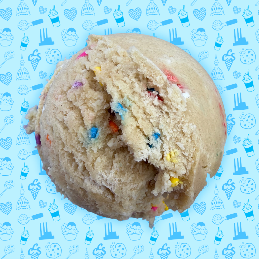 Birthday cake cookie dough scoop with colorful sprinkles and frosting ribbon mixed throughout on a blue Capital City Sweets patterned background.