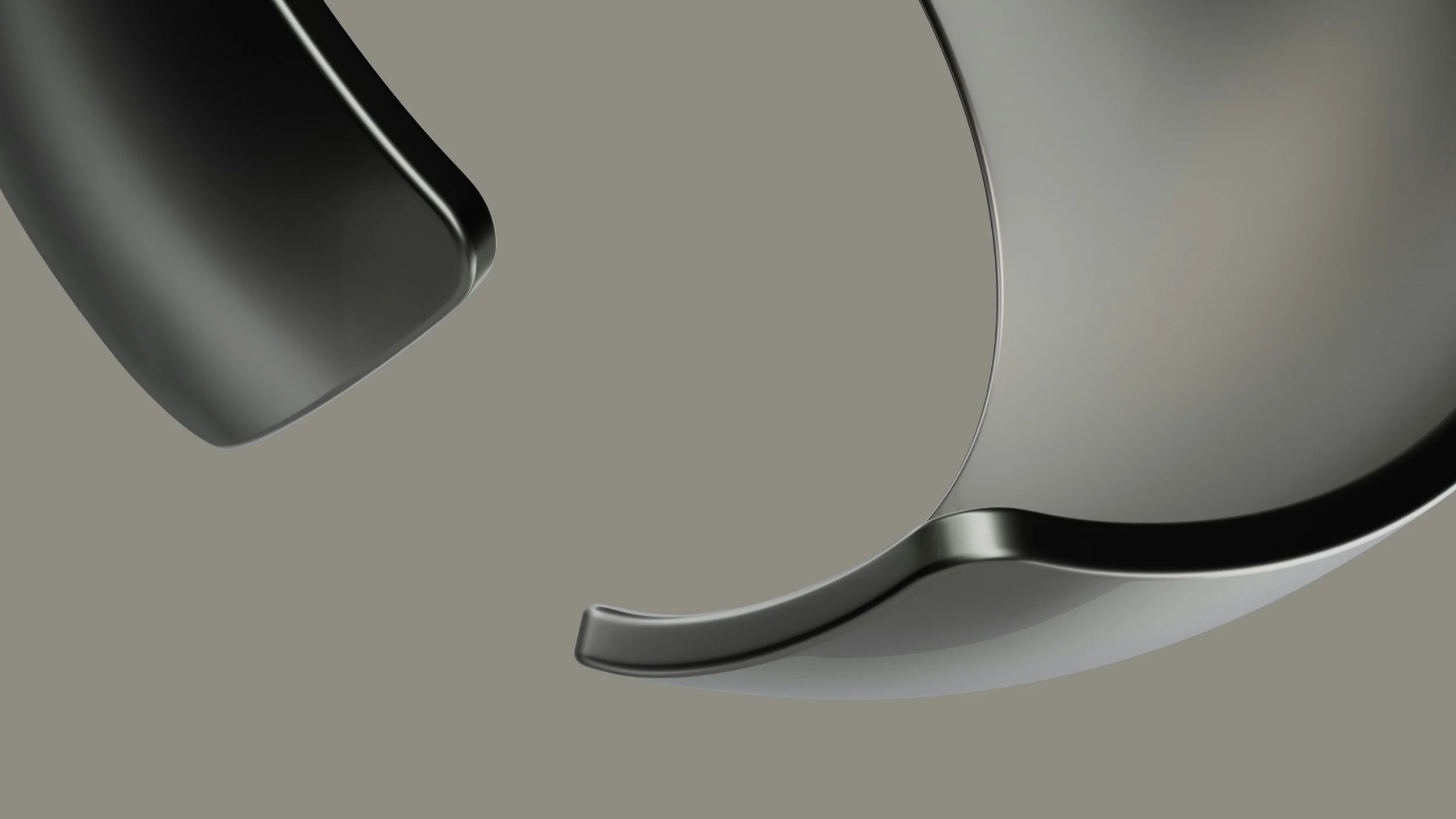 Close-up of a metallic, curved object with smooth, shiny surfaces against a grey background.