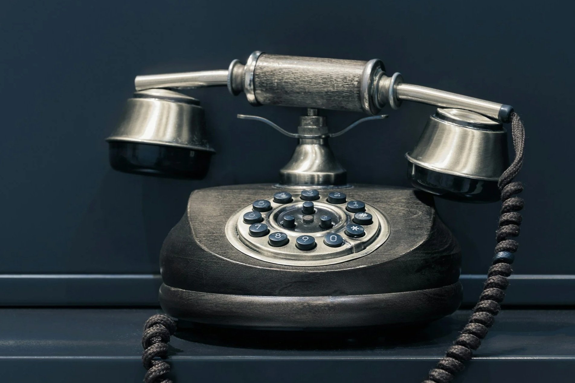 Vintage rotary telephone with metal and wood details, placed on a dark surface against a dark background.