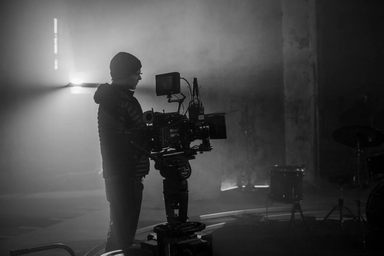 A camera's LCD screen shows a live view of a band performing, with two members playing guitars, in a dimly lit setting, with blurred individuals in the background.